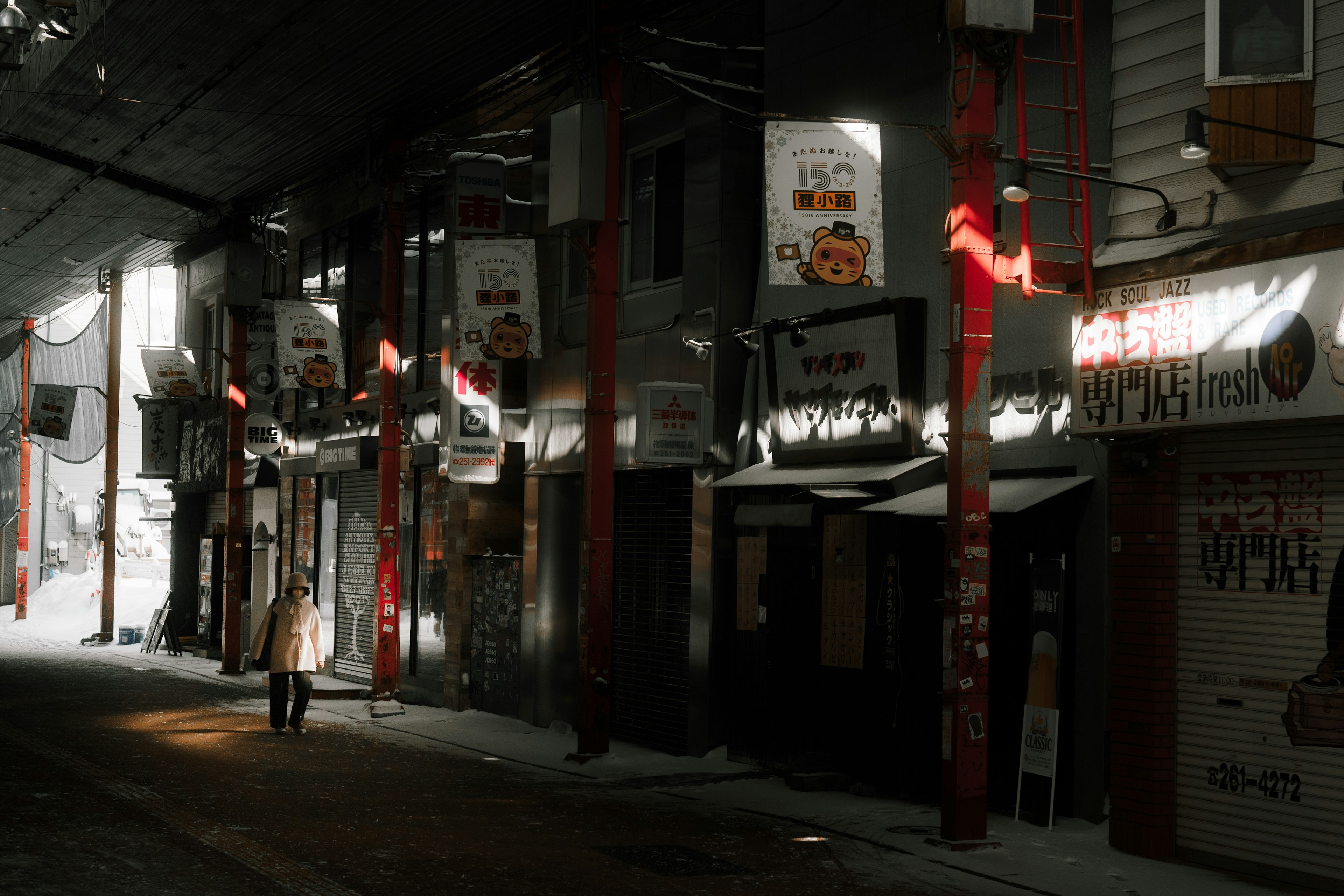 Dimly lit street with storefronts and a silhouette of a person