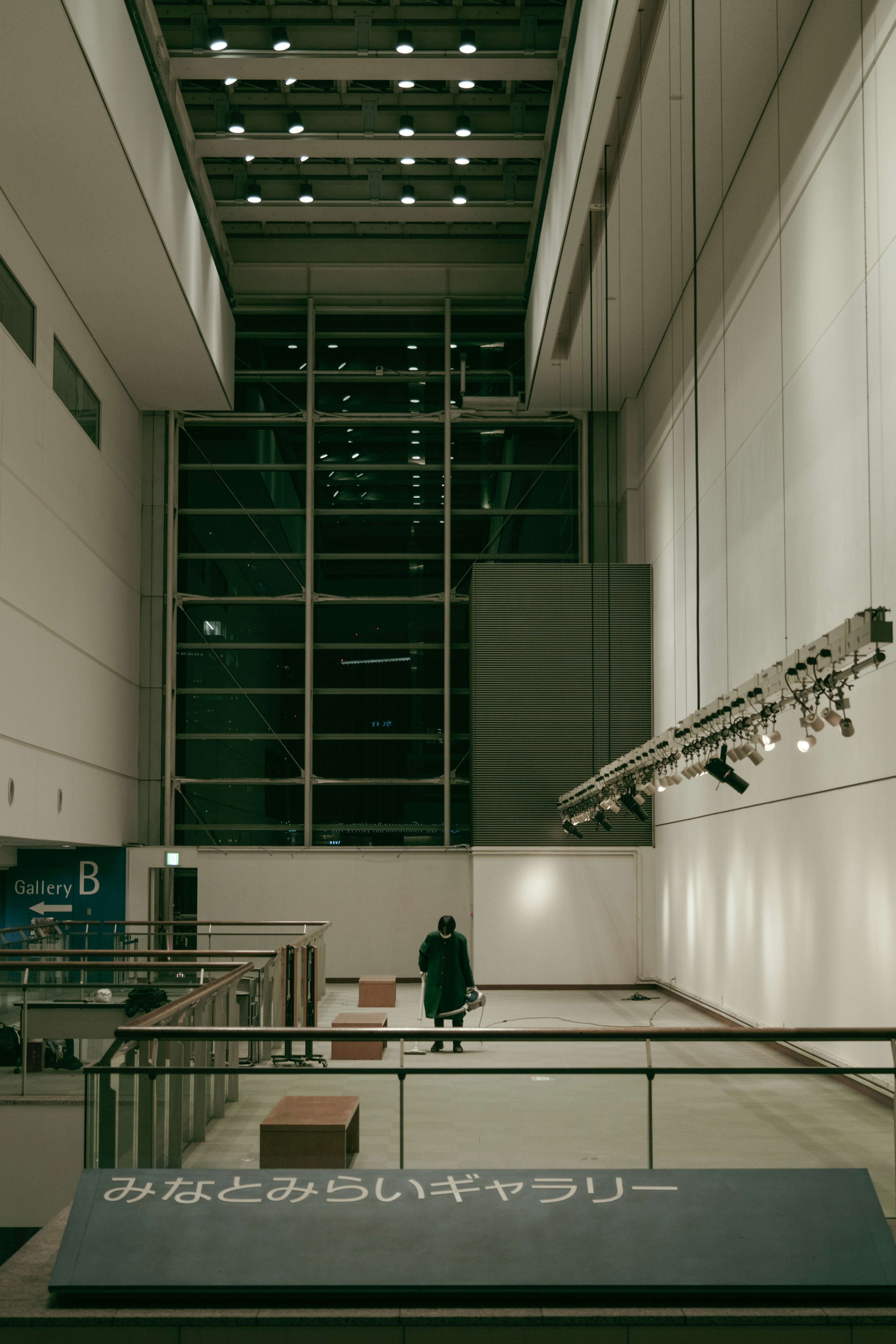 A spacious gallery interior with a lone figure walking under large windows allowing natural light