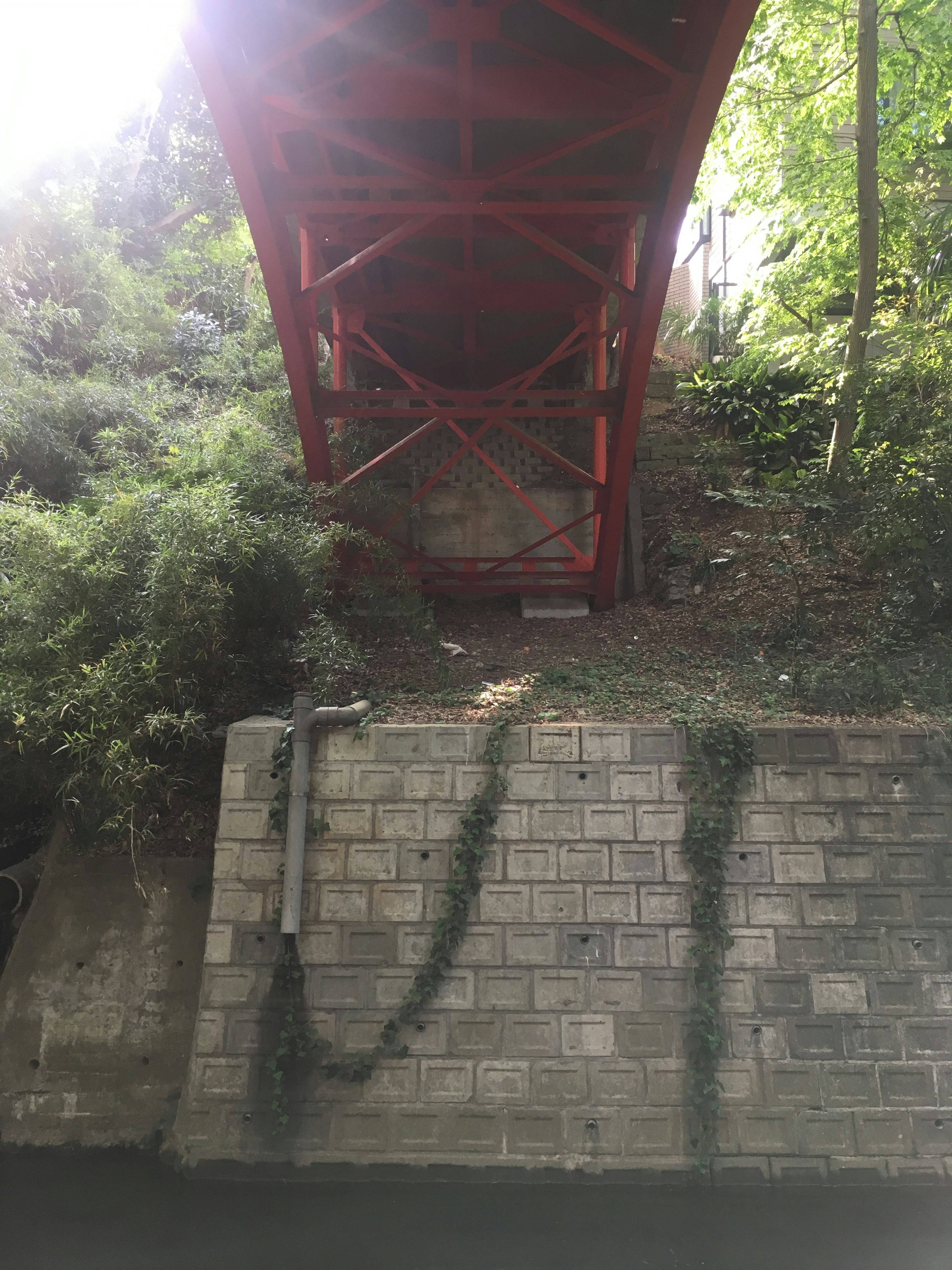 Red bridge spanning over lush greenery with stone wall