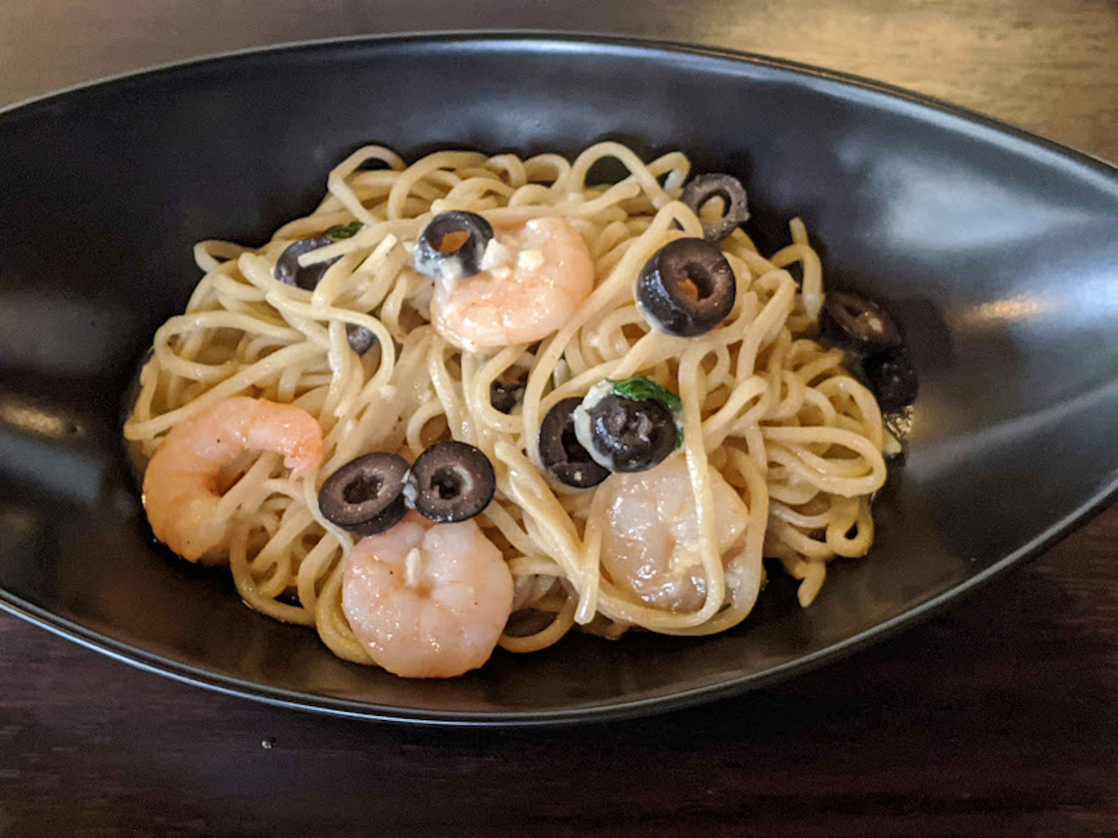 Spaghetti mit Garnelen und Oliven in einer schwarzen Schüssel serviert