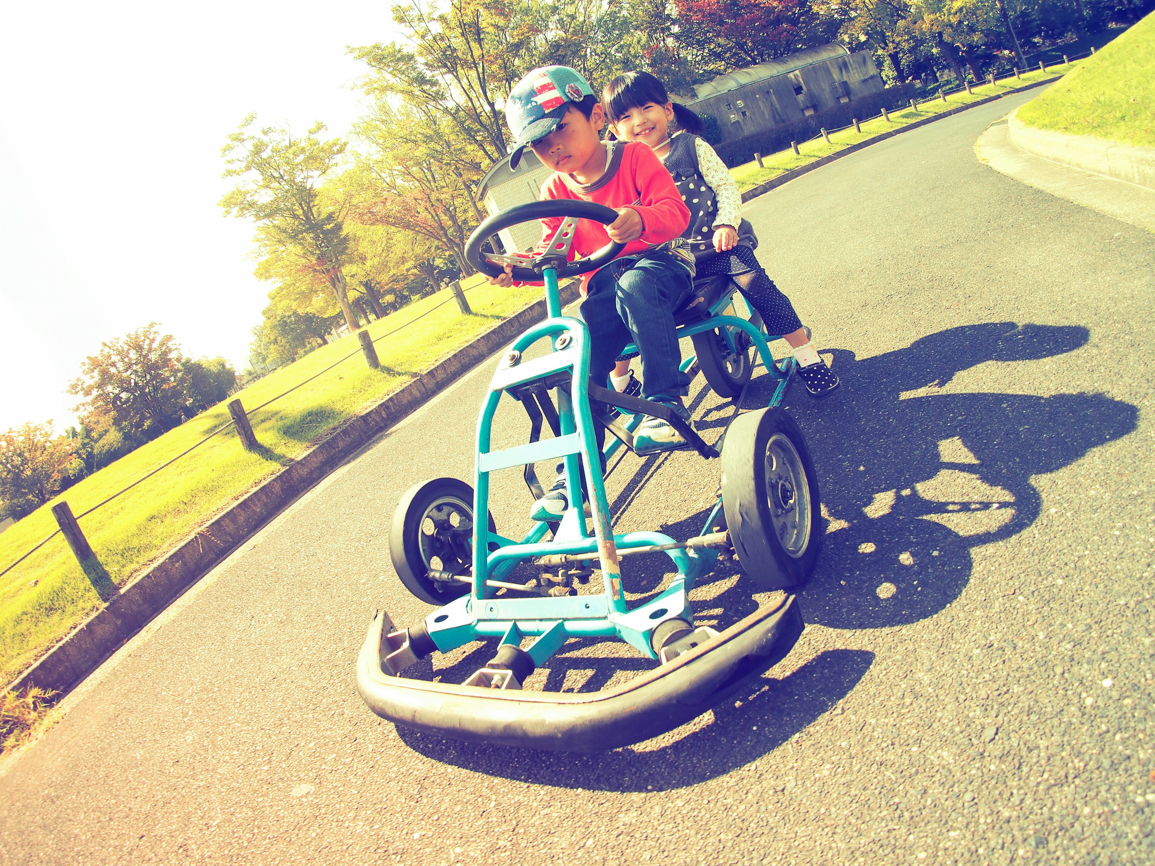 Children riding a blue go-kart on a park pathway