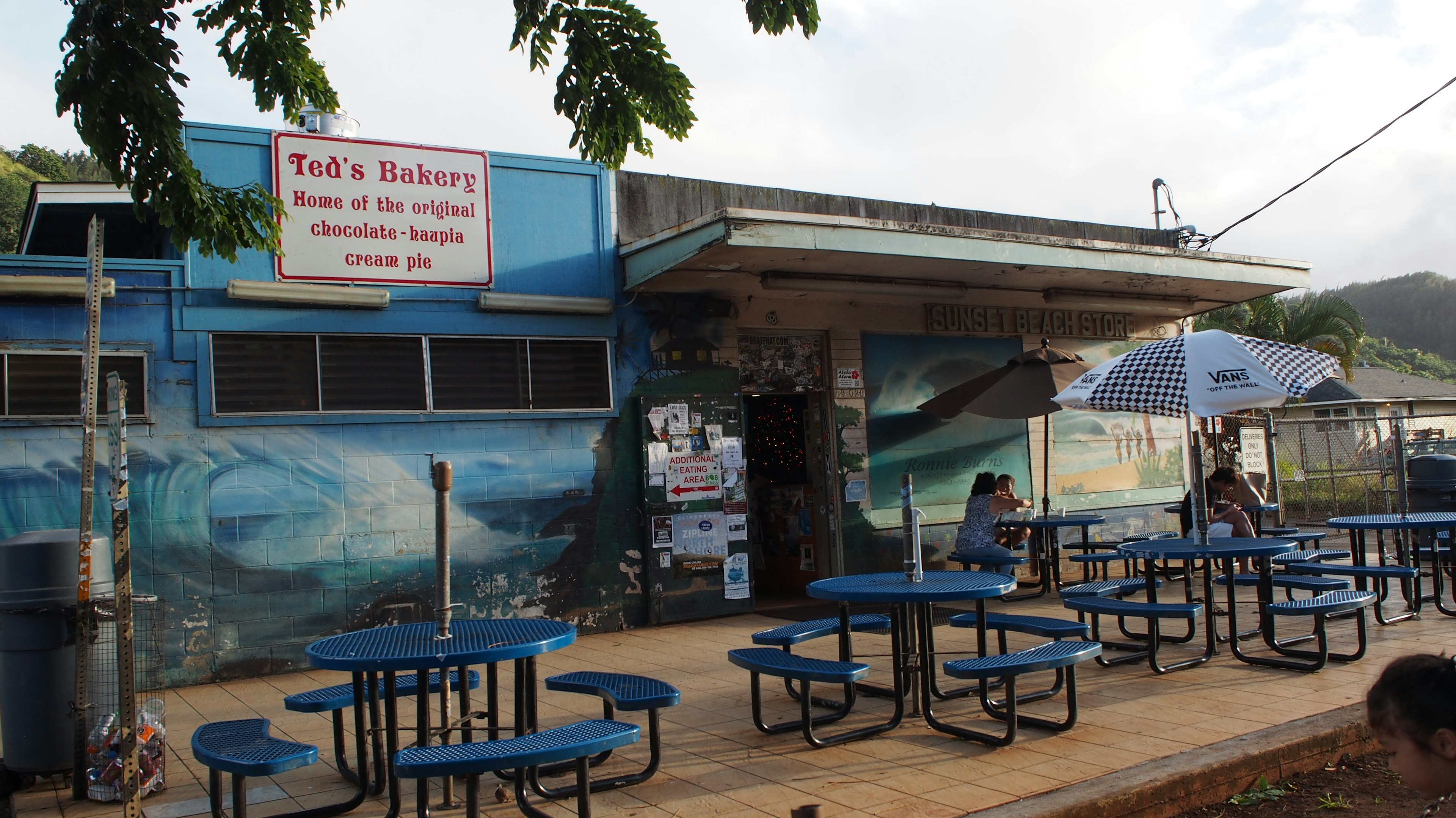 Tack's Barbecue asientos al aire libre con mesas y sillas azules frente a un mural