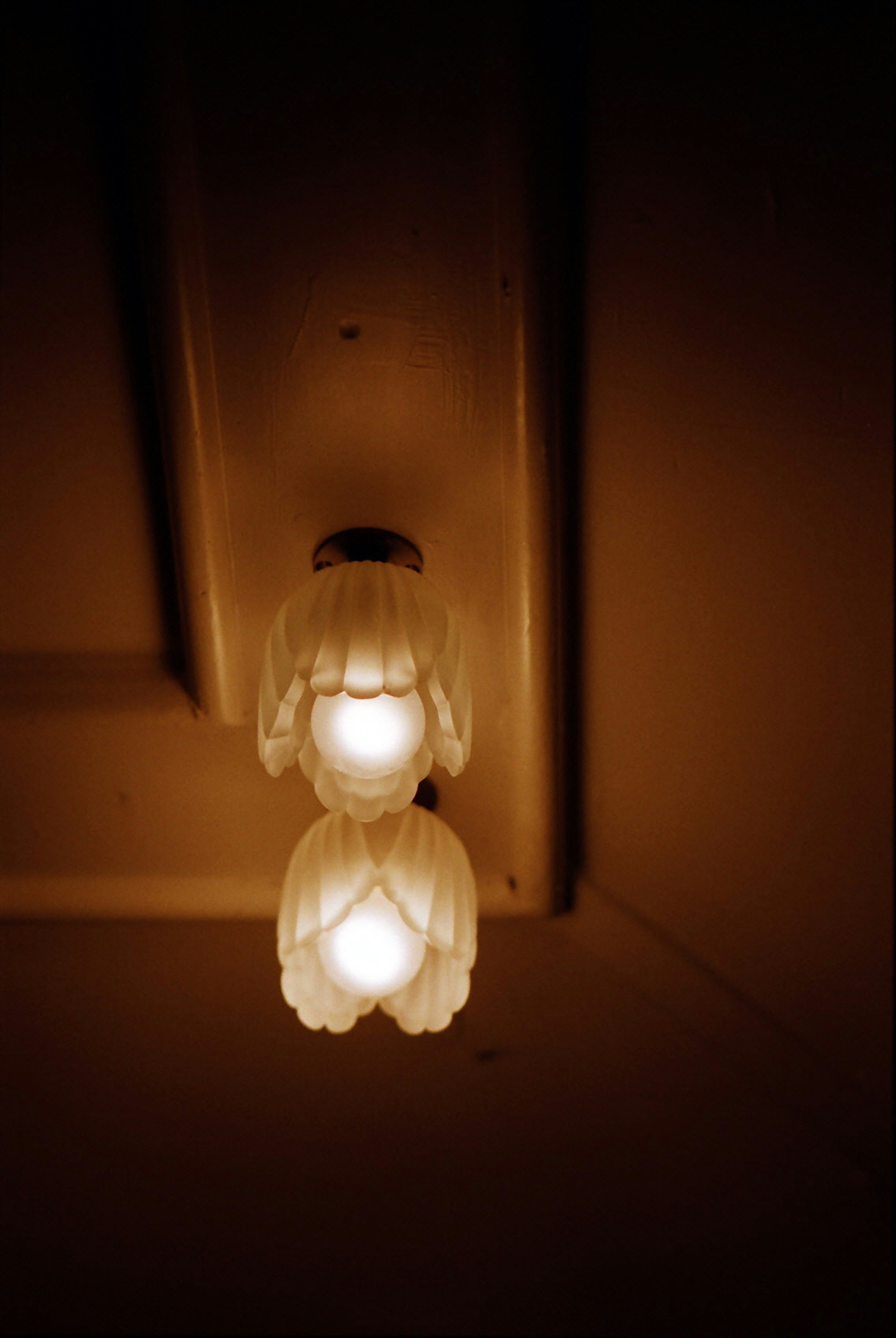 Image of two white lamp shades hanging from the ceiling in a dimly lit room