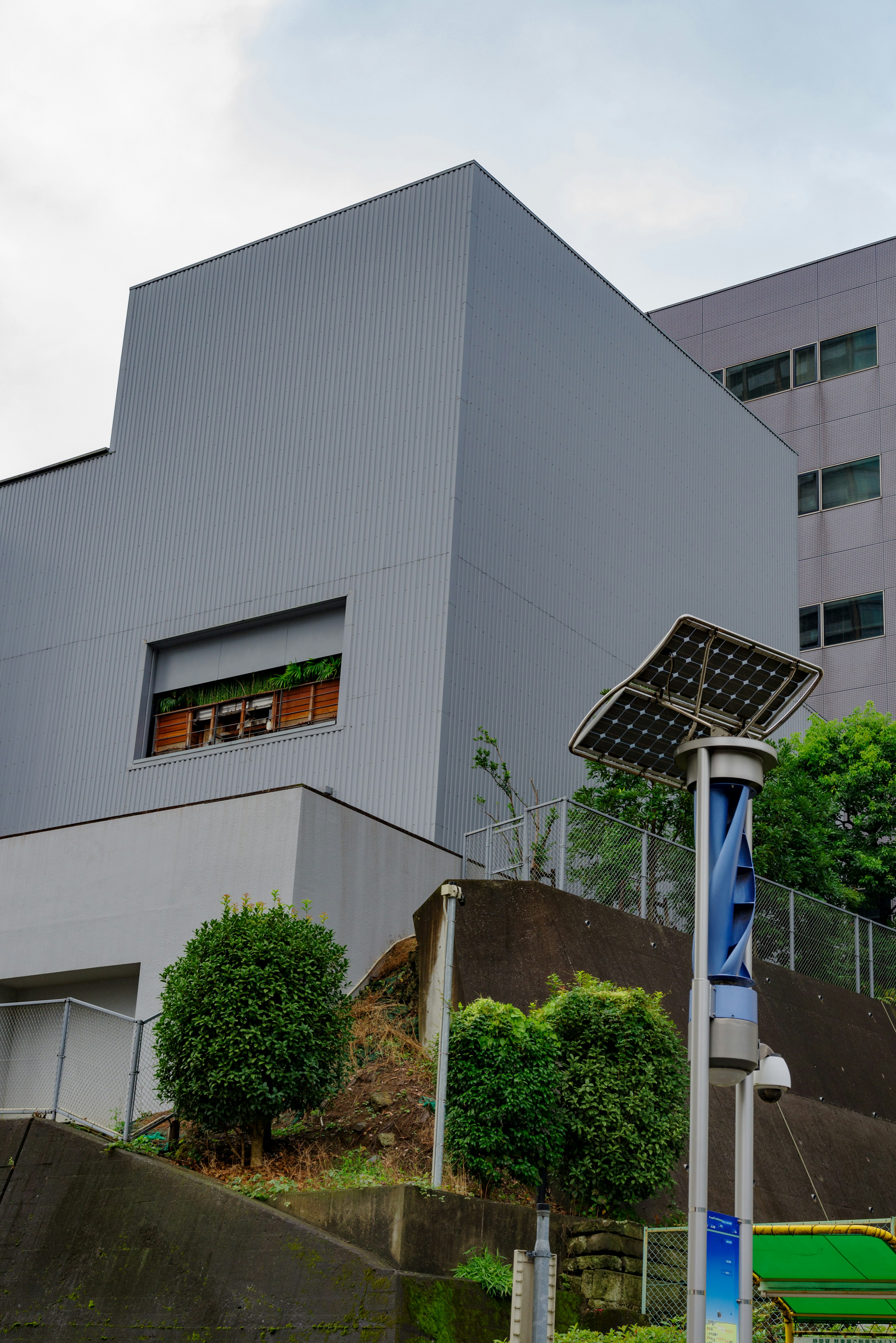 Edificio moderno gris con una ventana que muestra vegetación