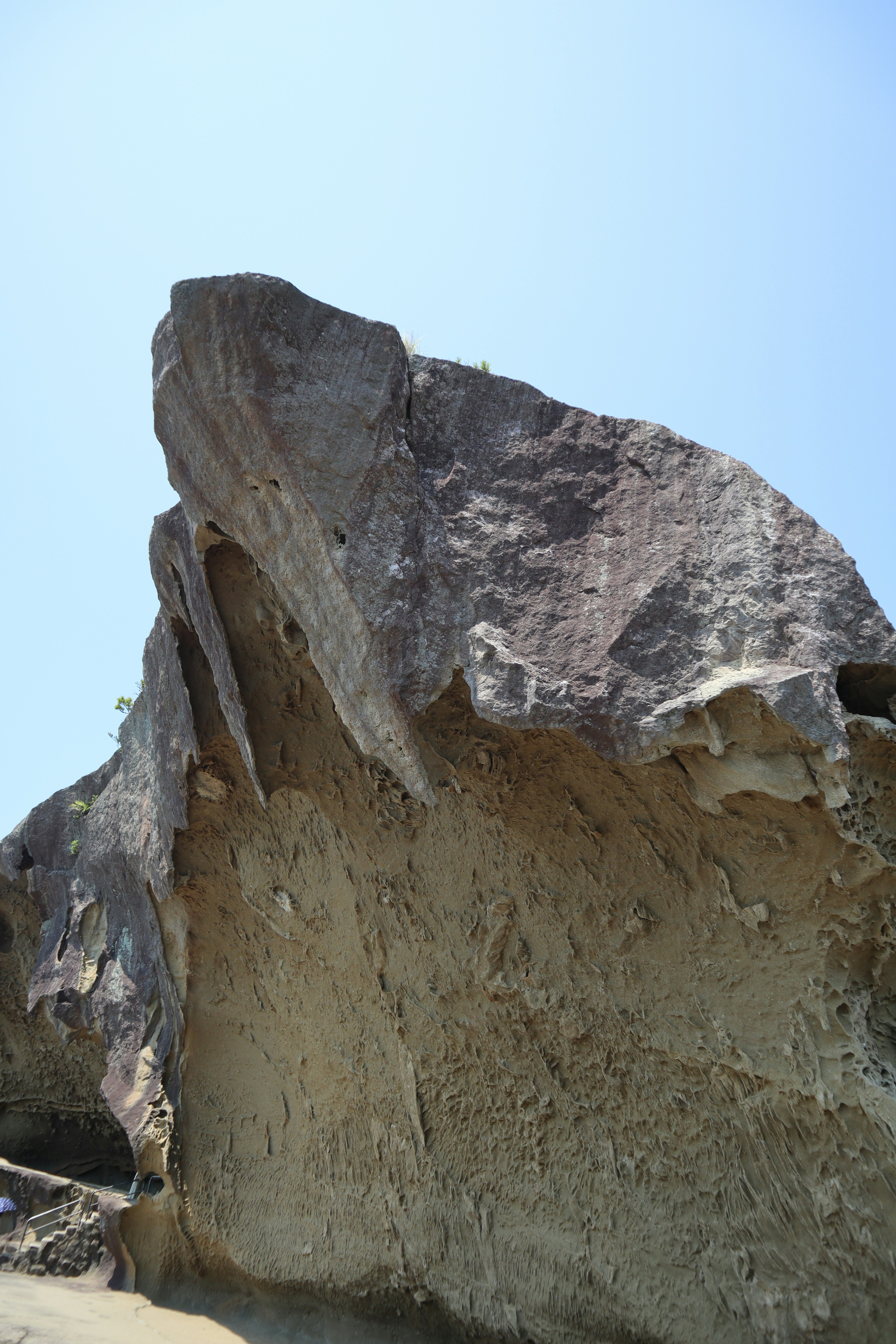 A large rock with a distinctive shape against a clear blue sky