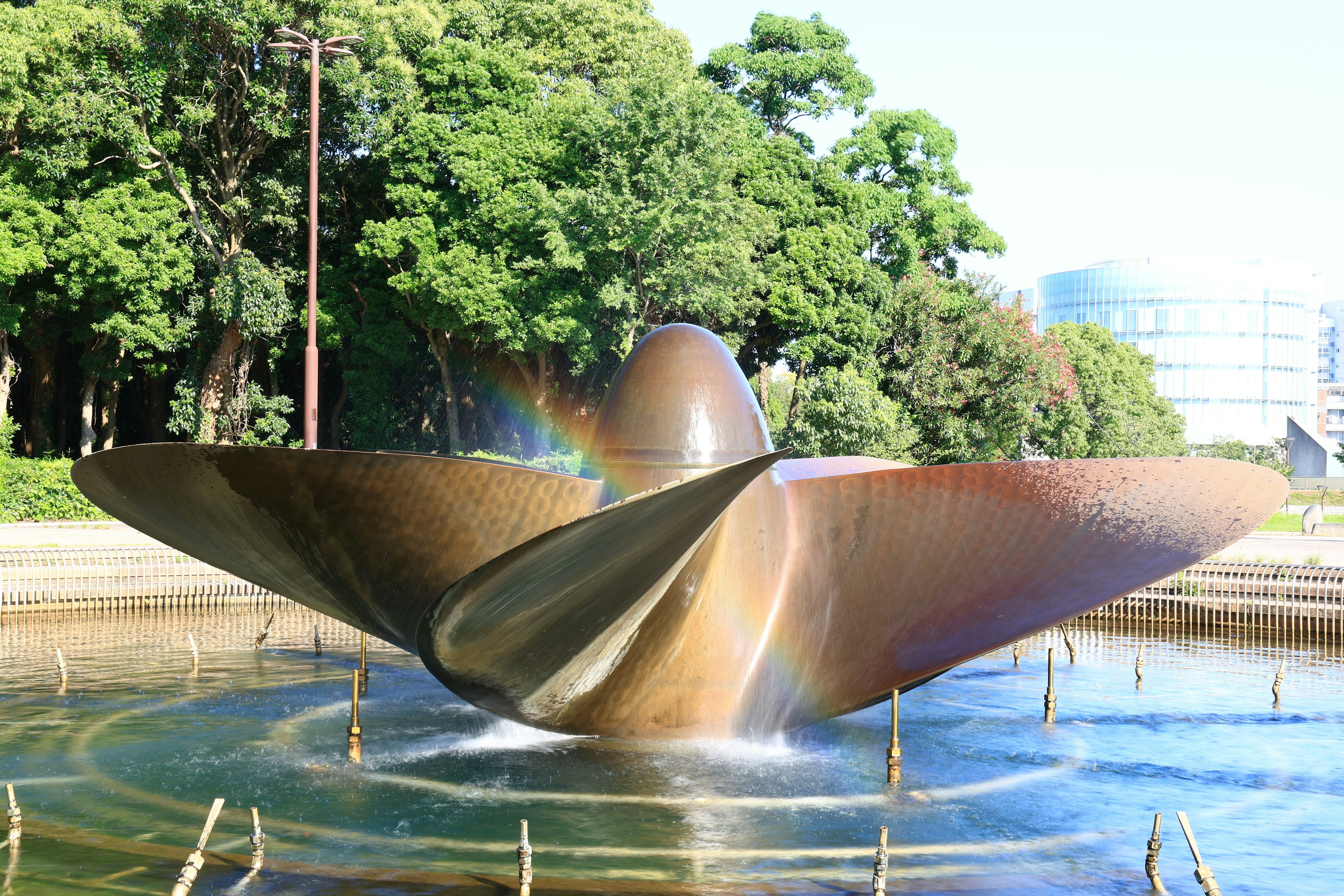 Escultura metálica abstracta en un estanque del parque rodeada de vegetación