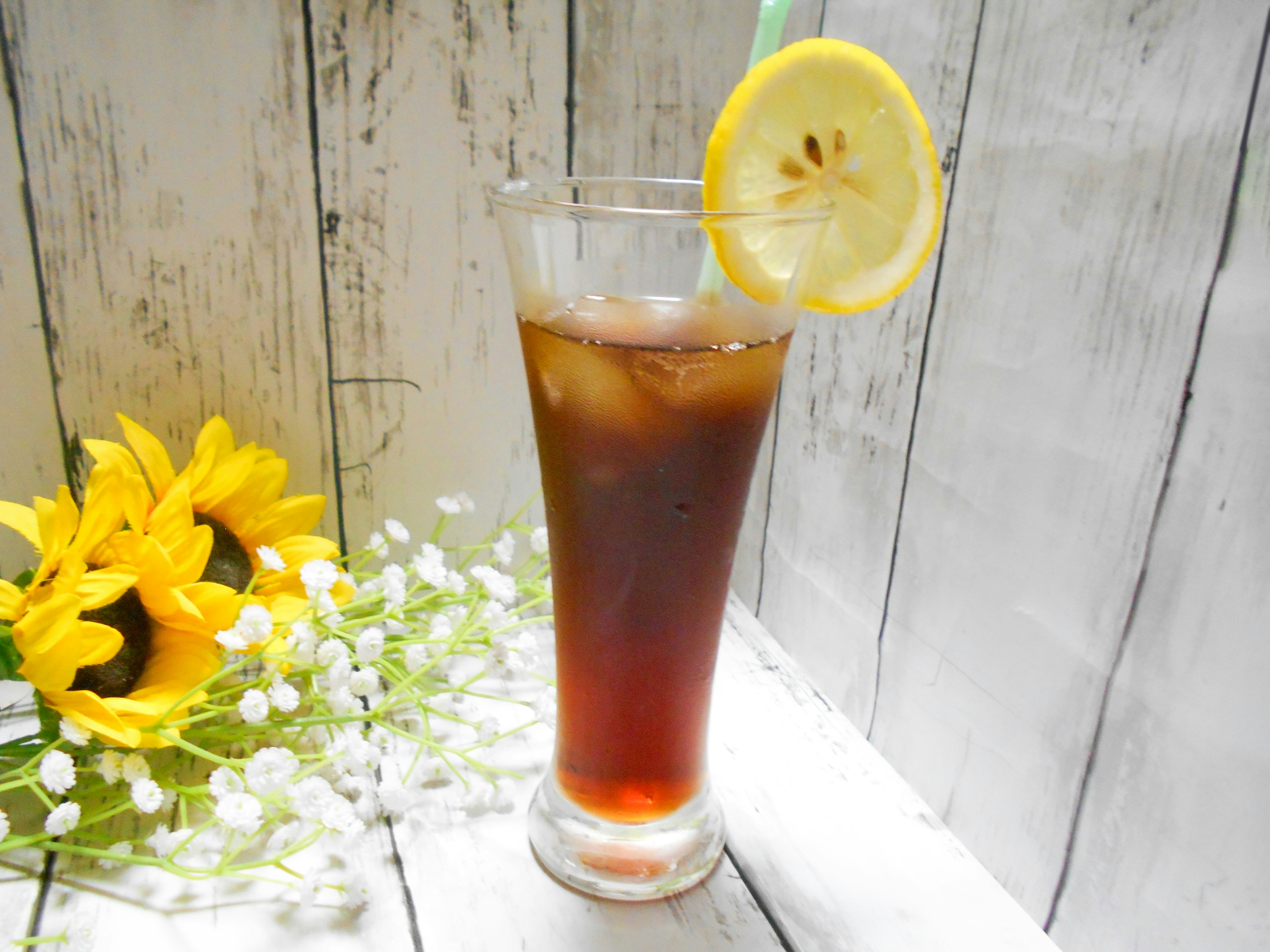 Glass of iced tea with lemon slice garnishing alongside sunflowers