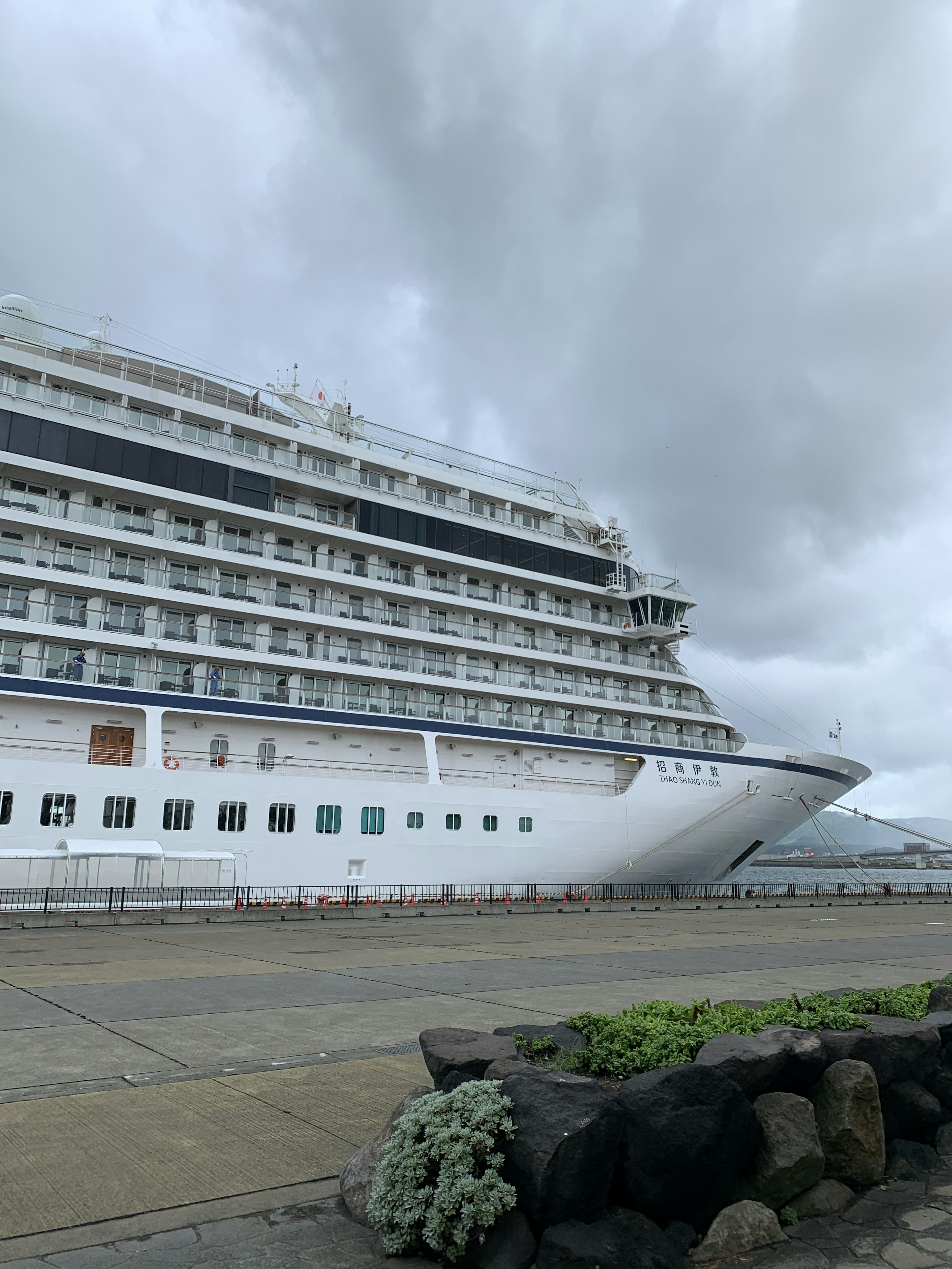 Grand navire de croisière amarré au port avec un ciel nuageux et une route pavée en arrière-plan