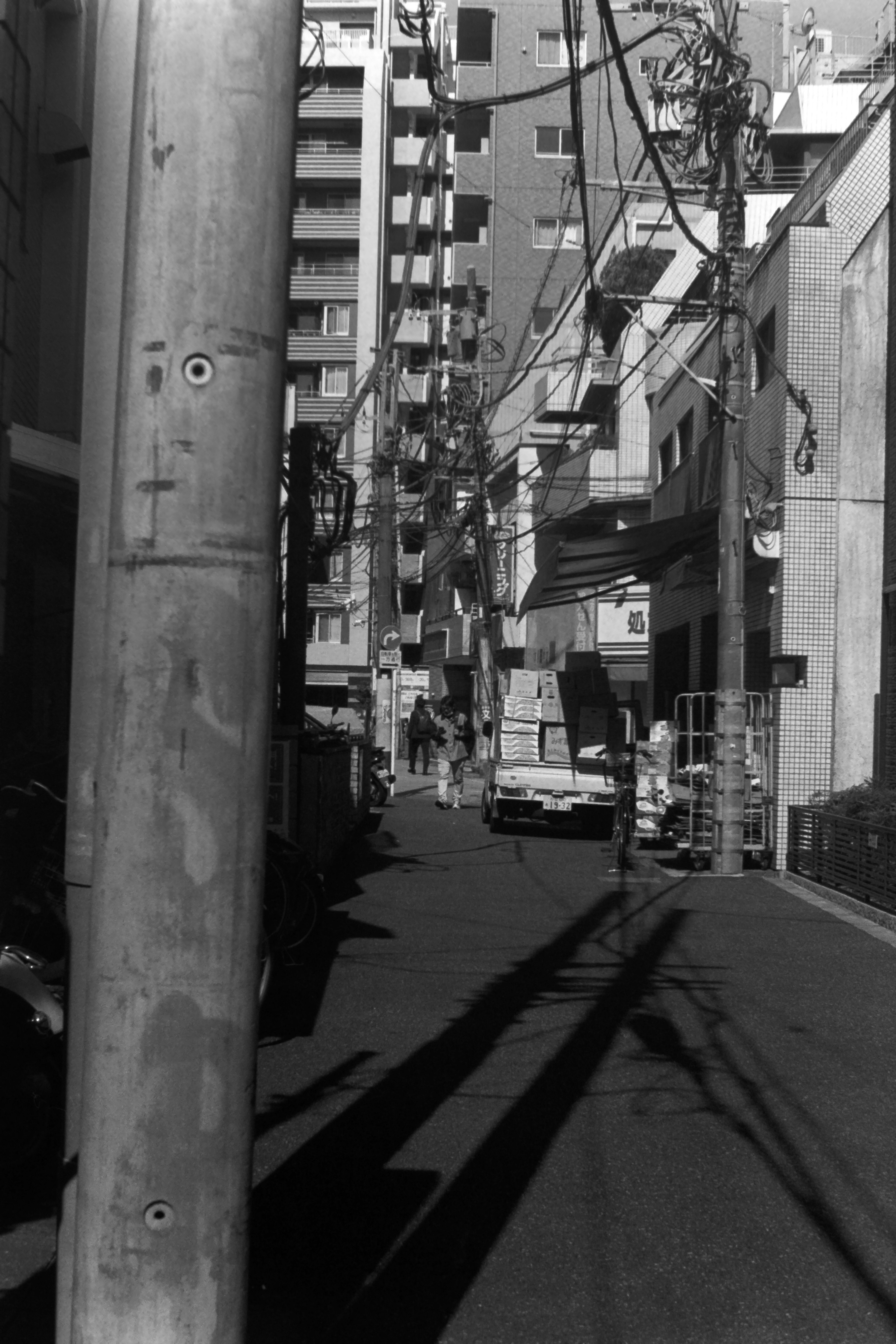 狭い路地に立つ電柱と影の写真 ビルが立ち並ぶ背景