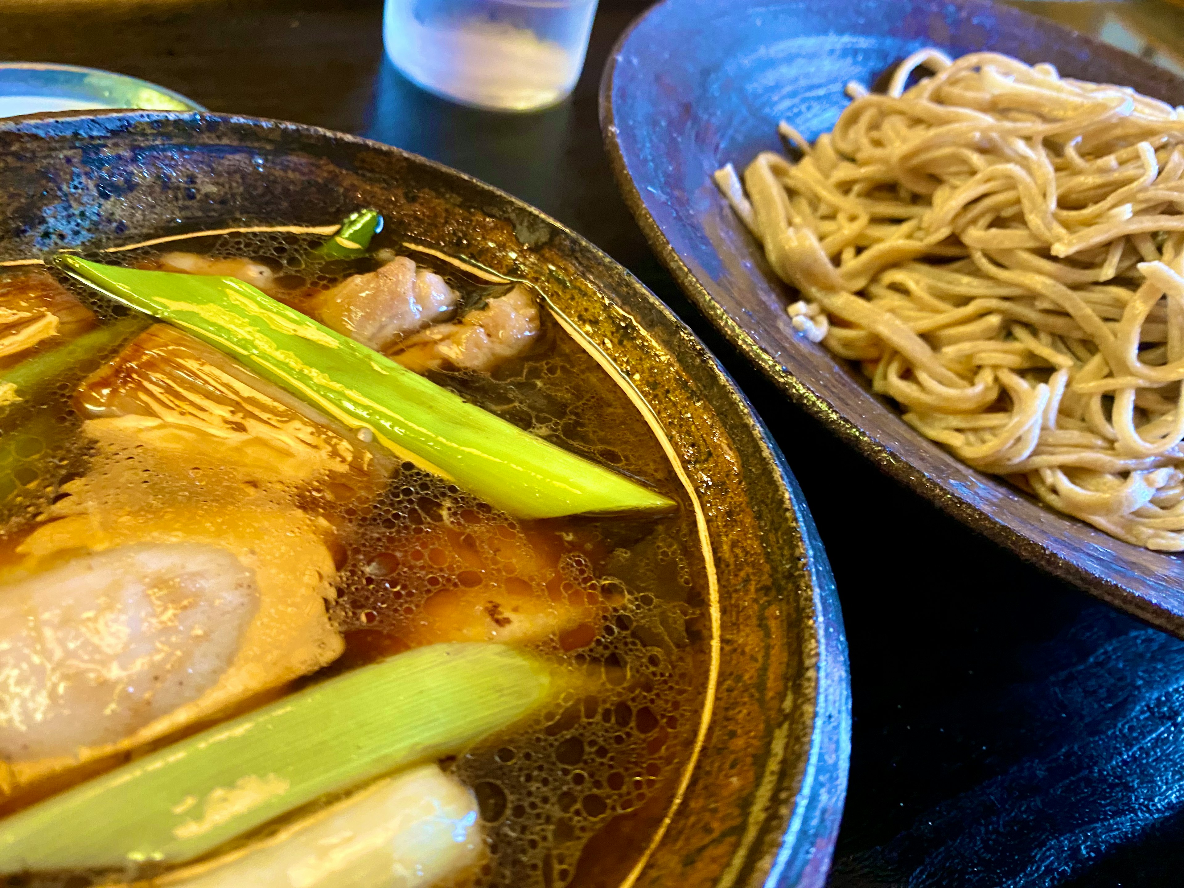 温かいスープの中にネギと肉が入った料理とそばの盛り付け