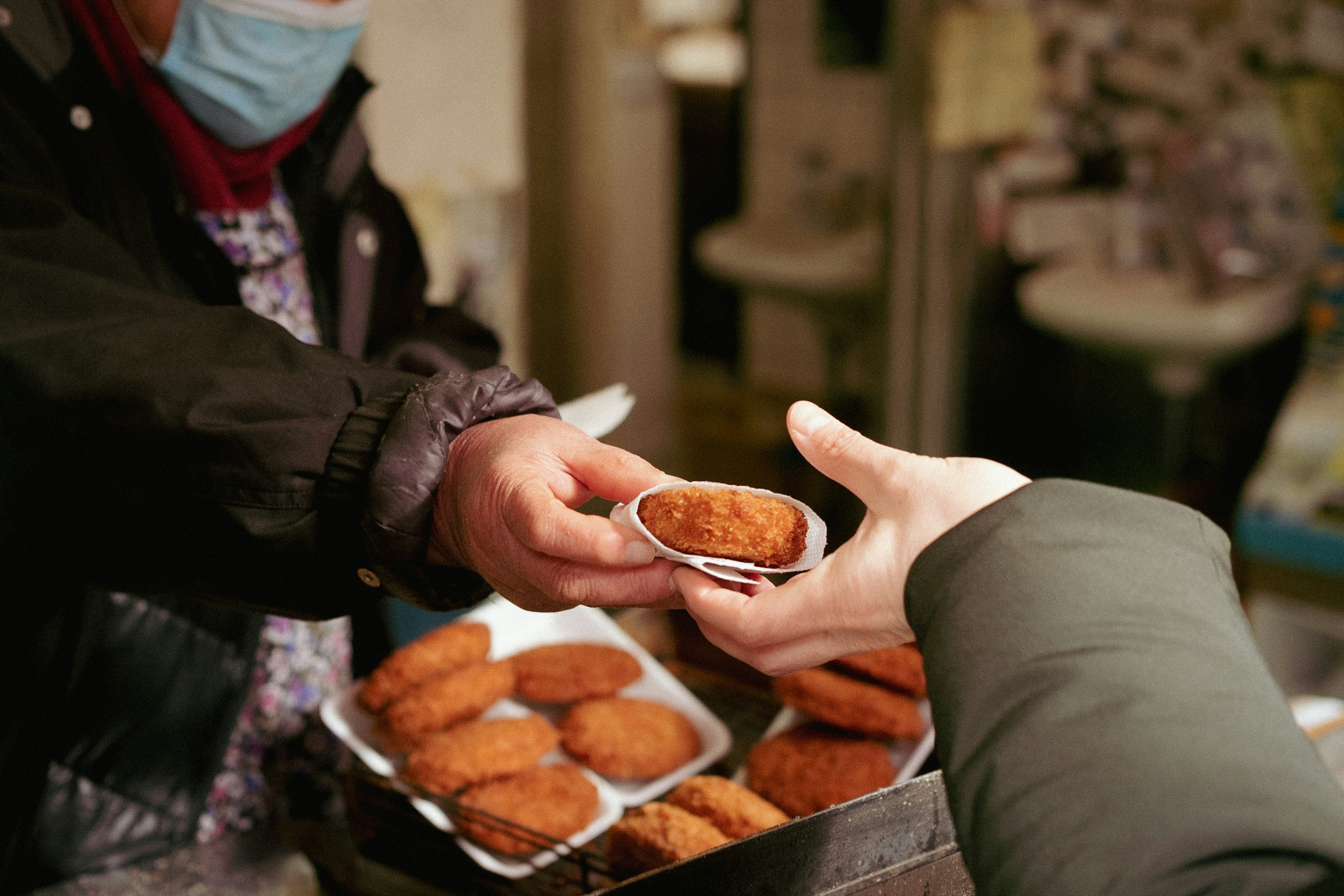 Seorang penjual menyerahkan kroket kepada pelanggan di pasar