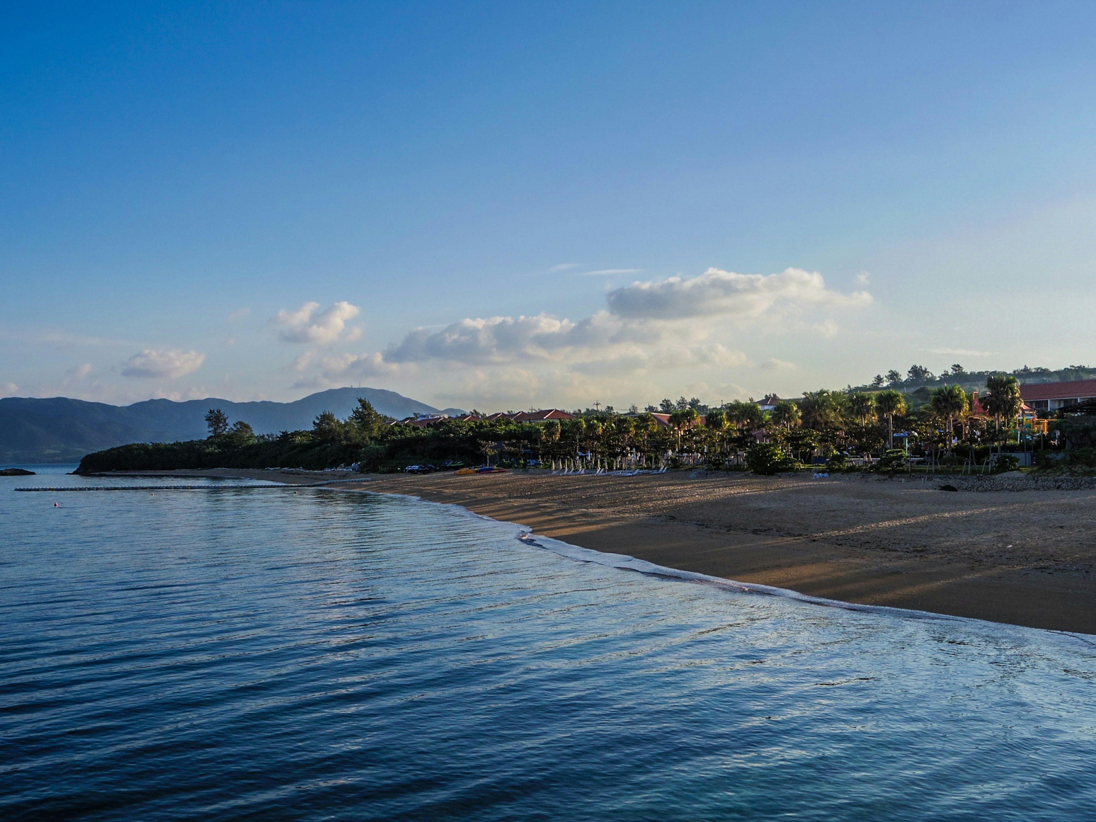 Pemandangan pantai yang tenang dengan air tenang dan bukit jauh