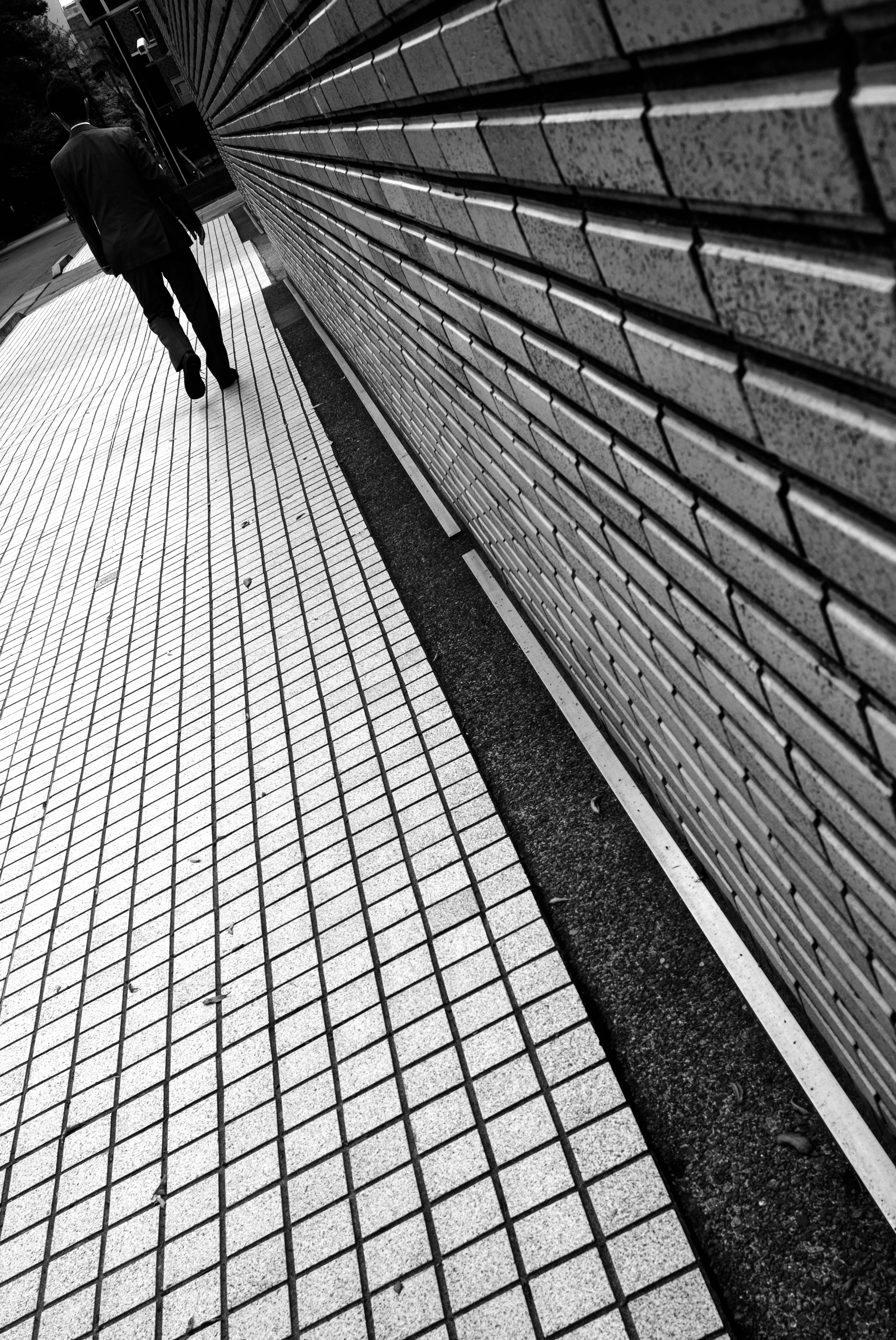 Monochrome street scene with a person walking along a wall