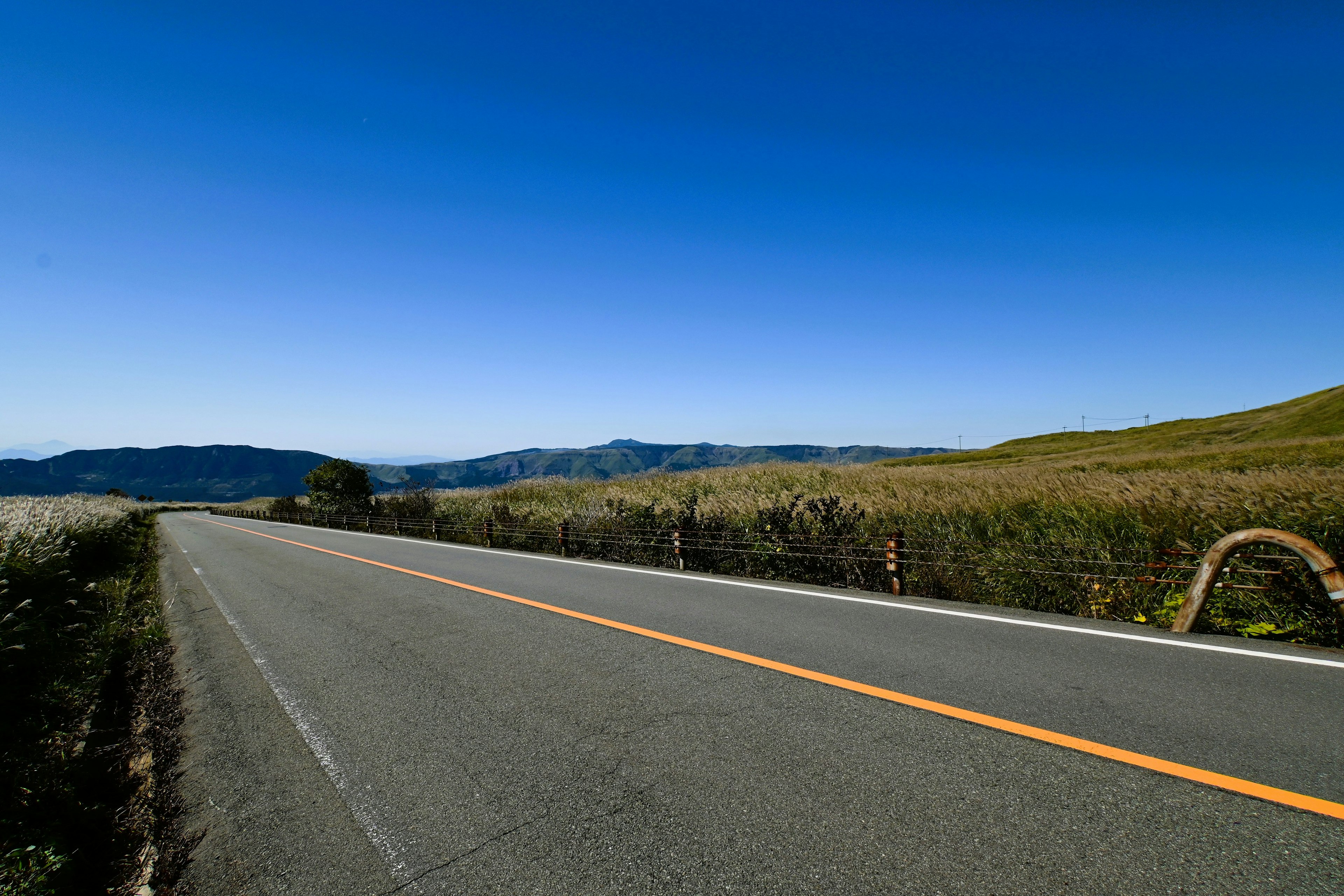 Paved road stretching through grassy landscape under blue sky