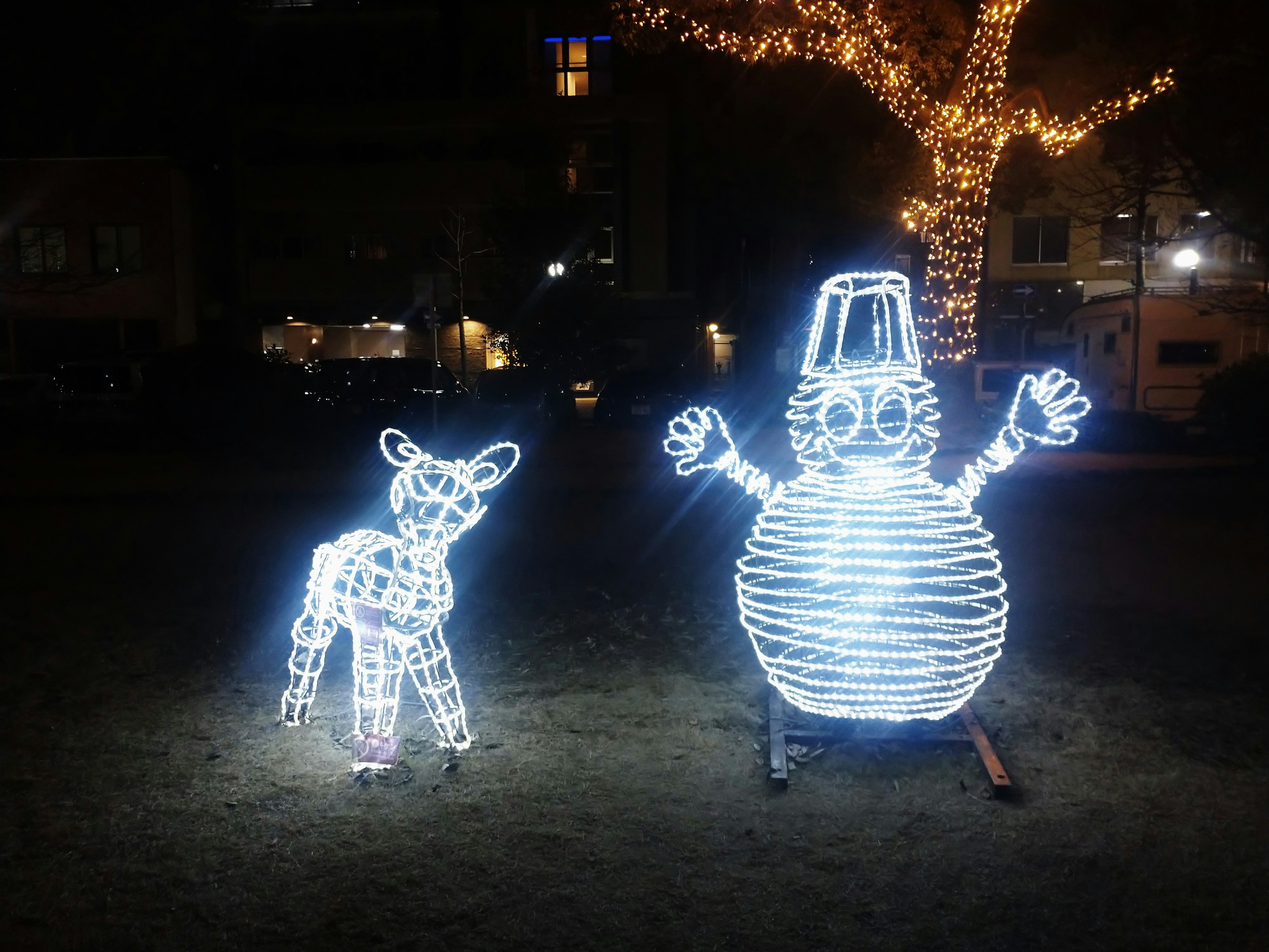 夜の公園に設置された光る白い鹿と雪だるま