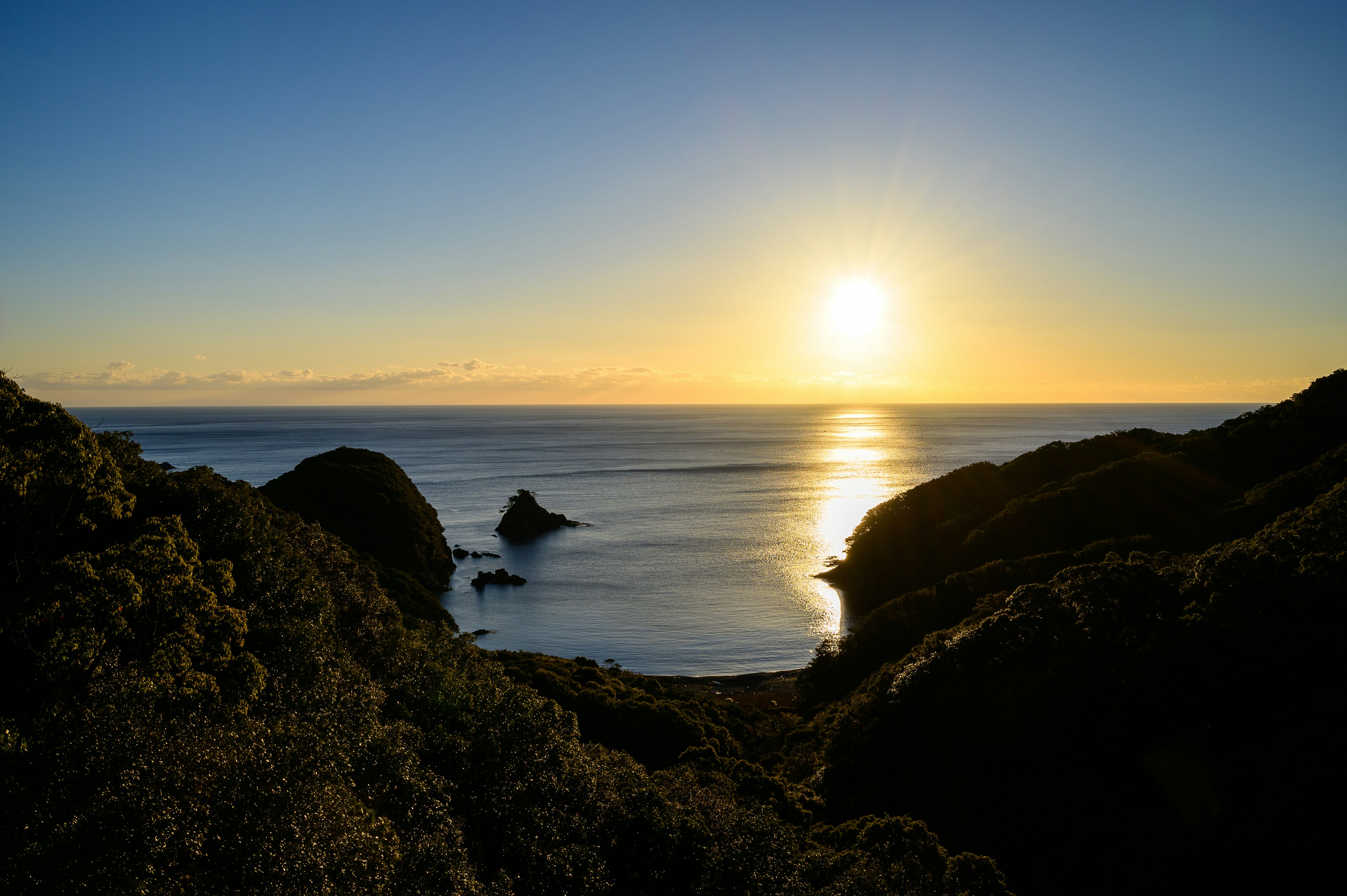 太陽が海に沈む美しい景色 緑の丘と静かな海