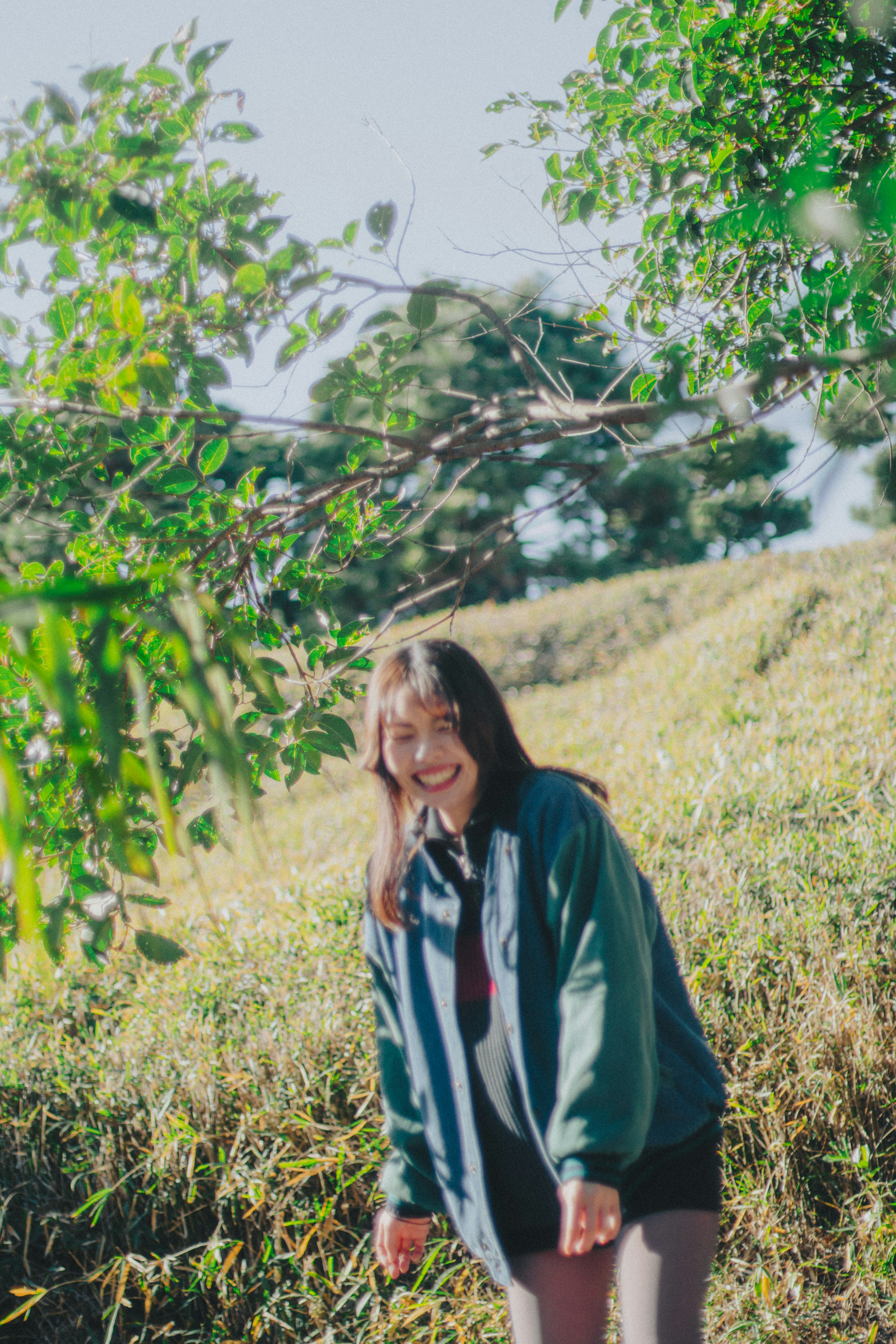 Seorang wanita tersenyum berdiri di antara daun hijau di ladang yang cerah