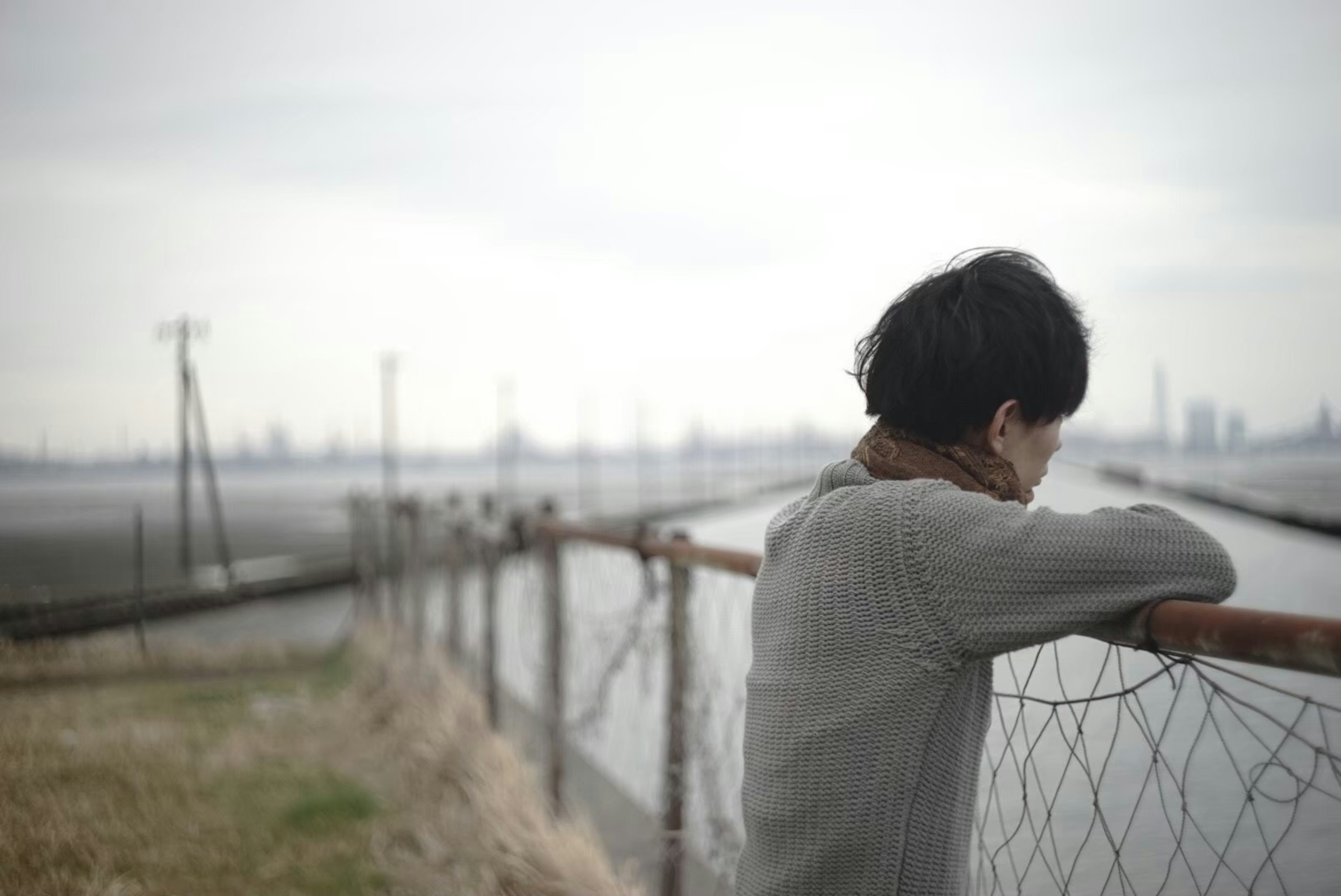 Un joven apoyado en una cerca bajo un cielo gris