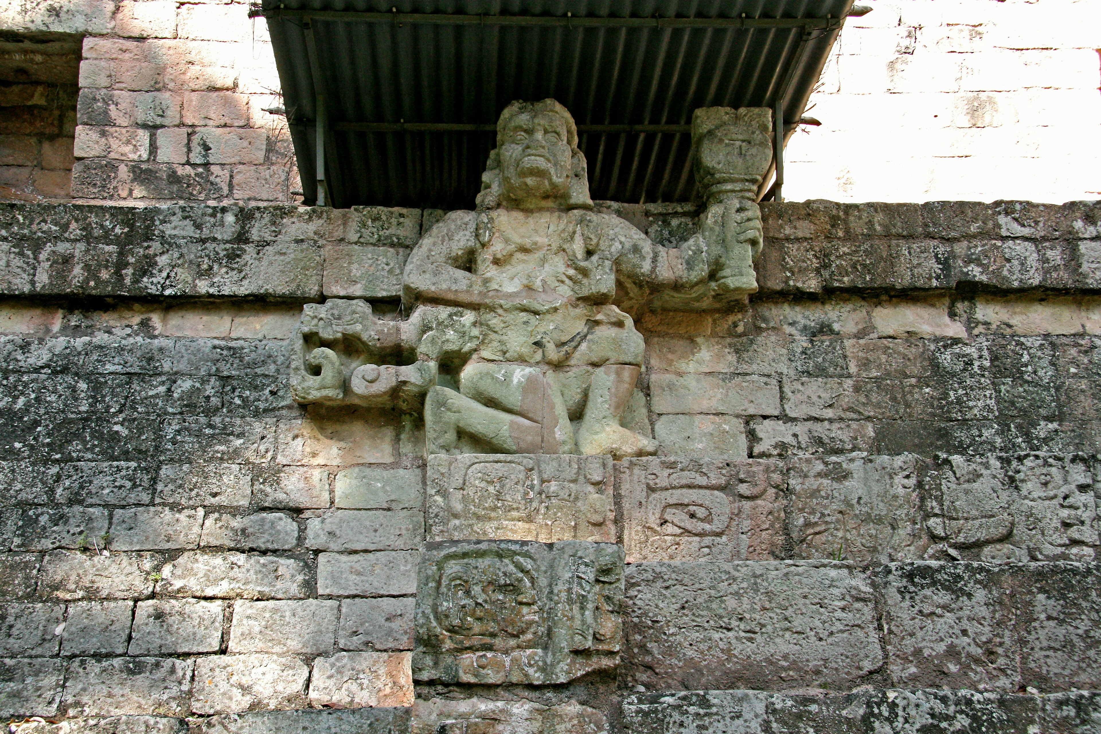 Antike Steinskulptur an einer Wand montiert, die eine Figur darstellt, die ein Objekt hält