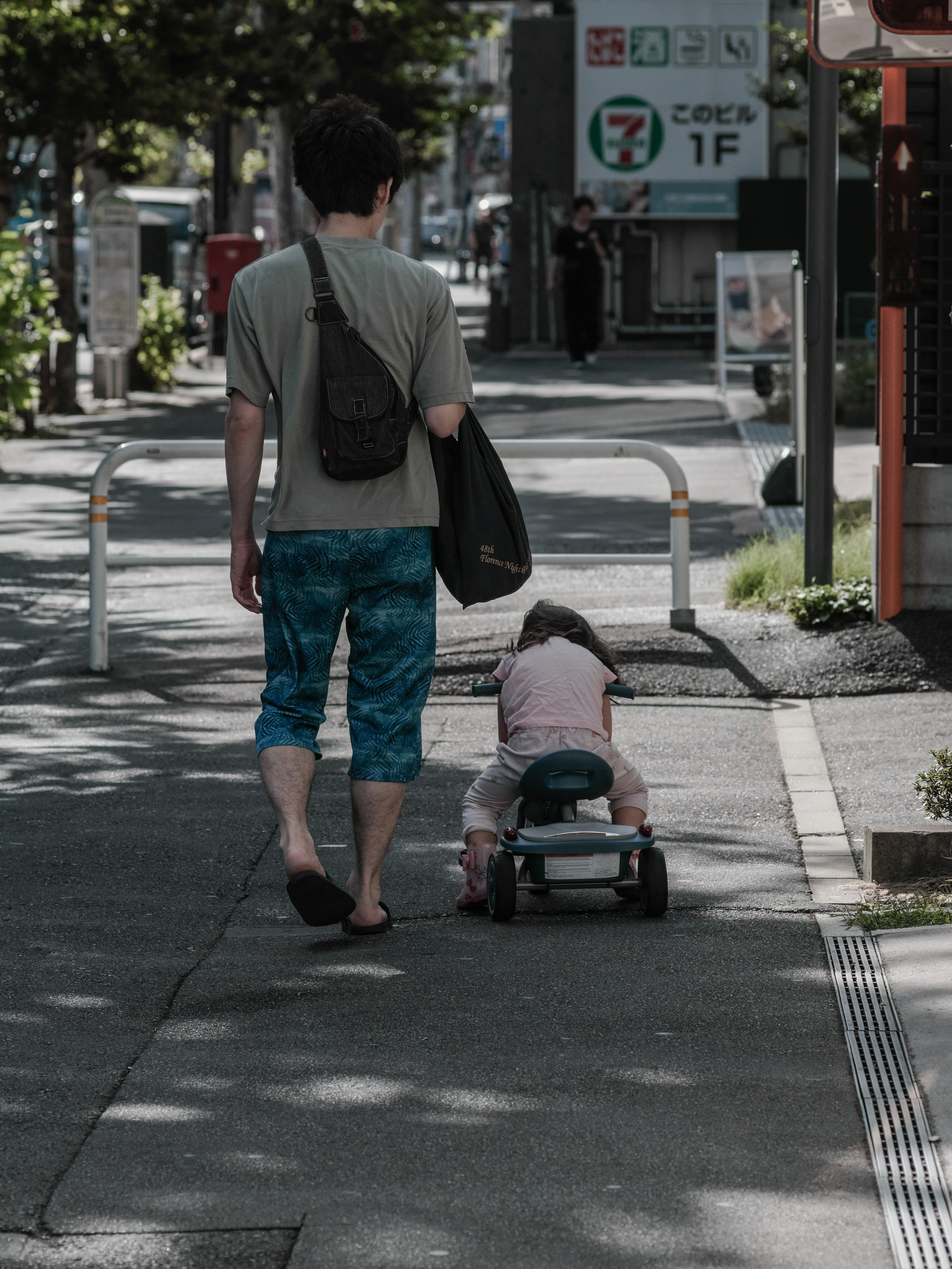 父親和孩子在人行道上走 孩子坐在玩具車上