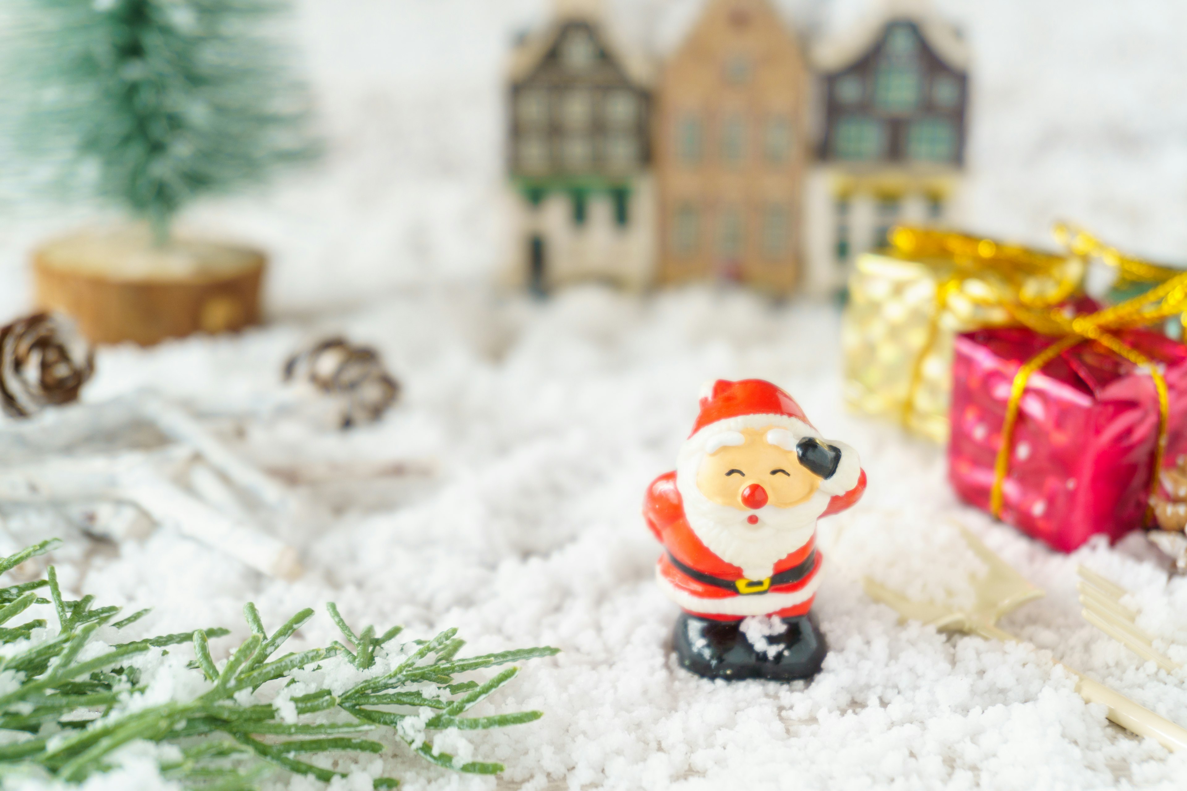 Figurina di Babbo Natale in piedi sulla neve con piccole scatole regalo e un albero di Natale