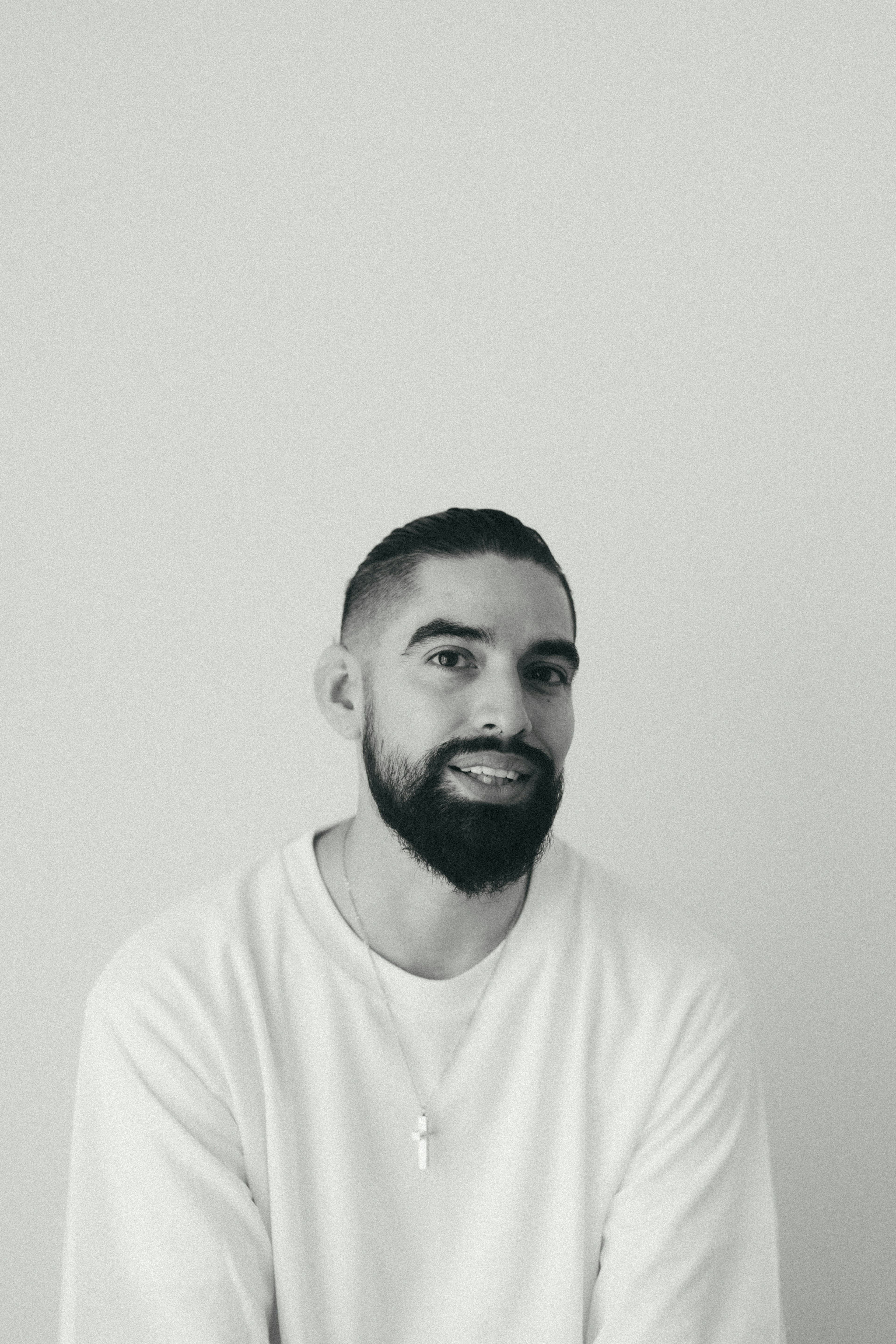 Un hombre sonriendo con una camisa blanca frente a un fondo simple