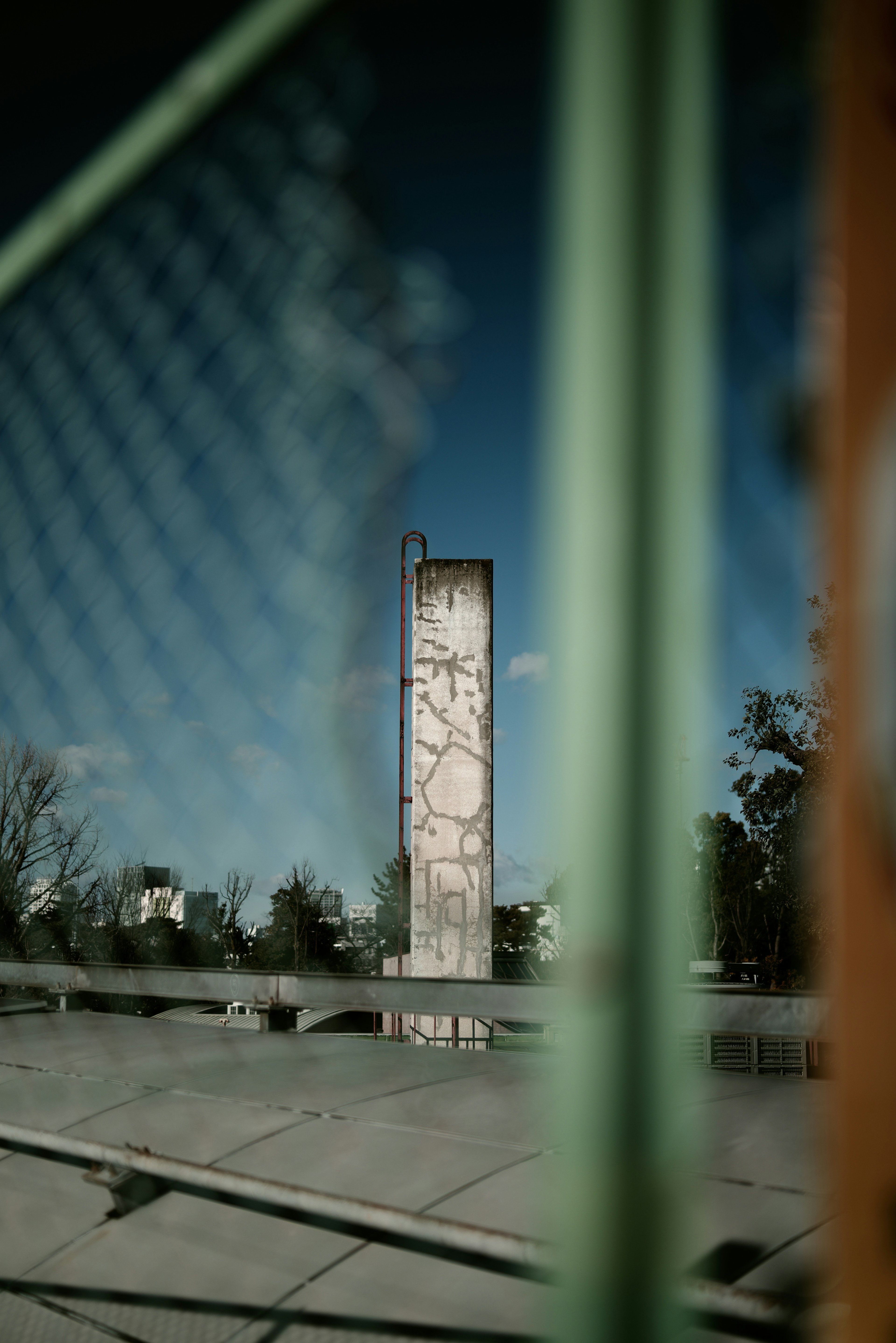 Alta torre de concreto visible a través de una cerca verde con cielo azul