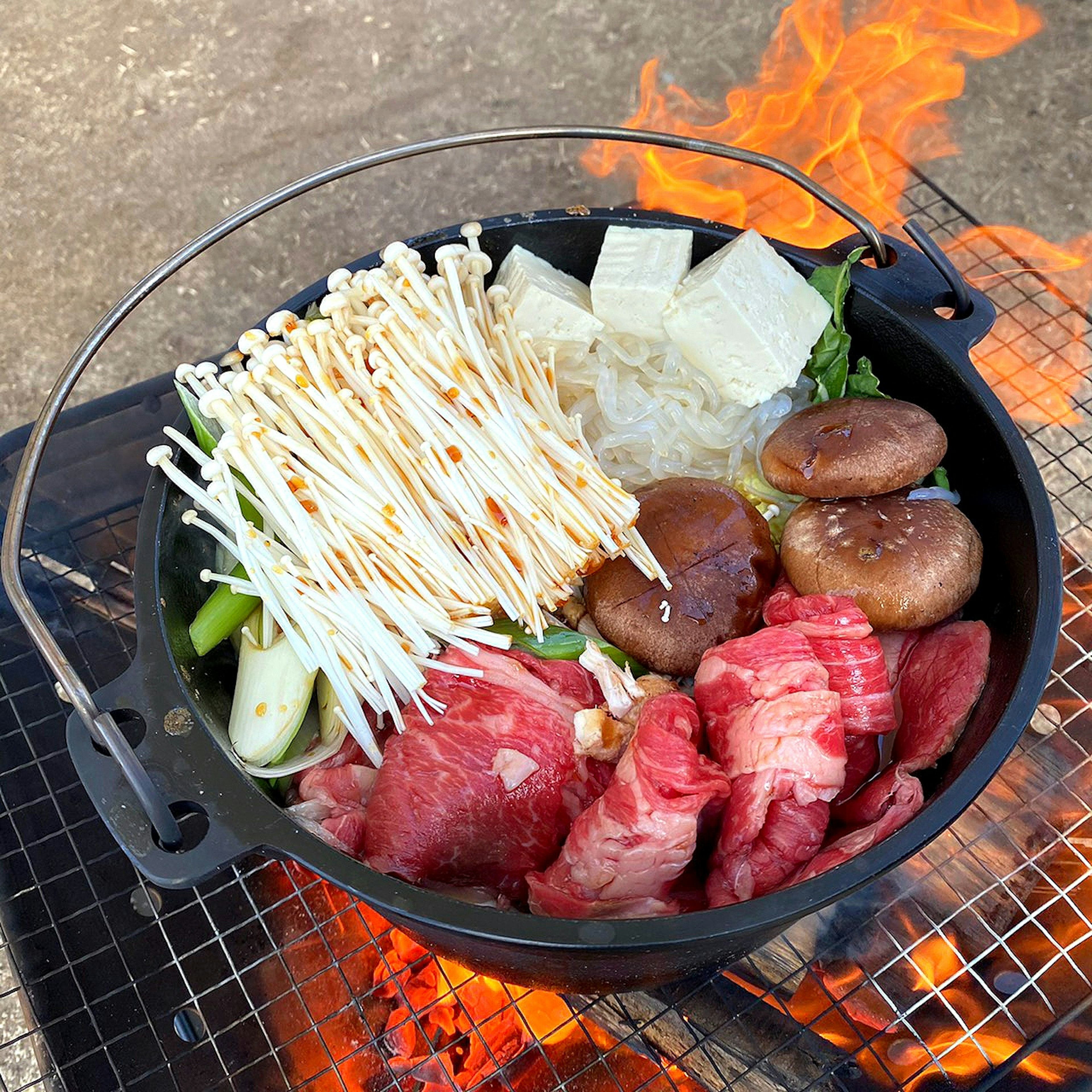 A pot filled with various ingredients for hot pot cooking over an open flame