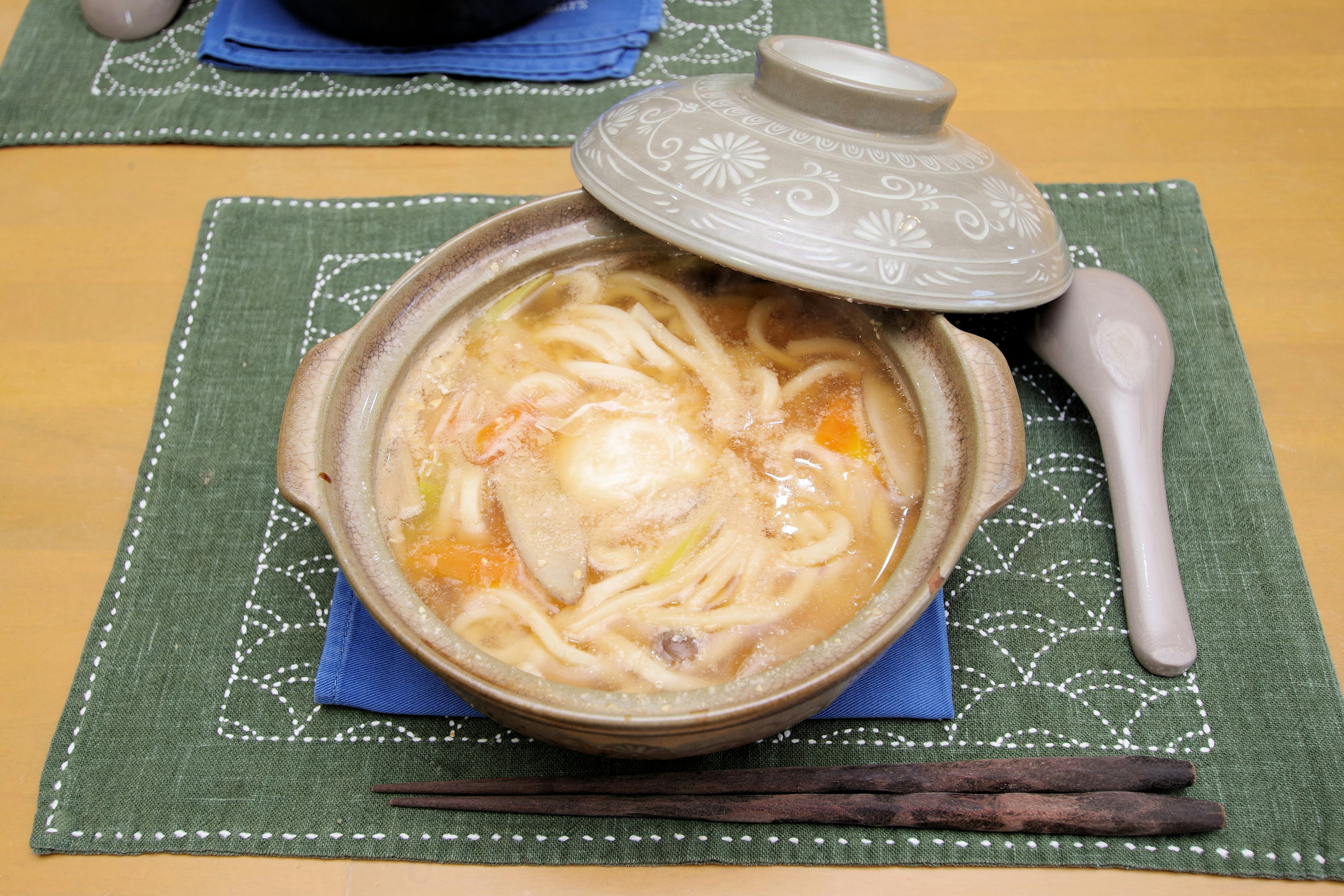 A warm pot dish featuring udon noodles and an egg