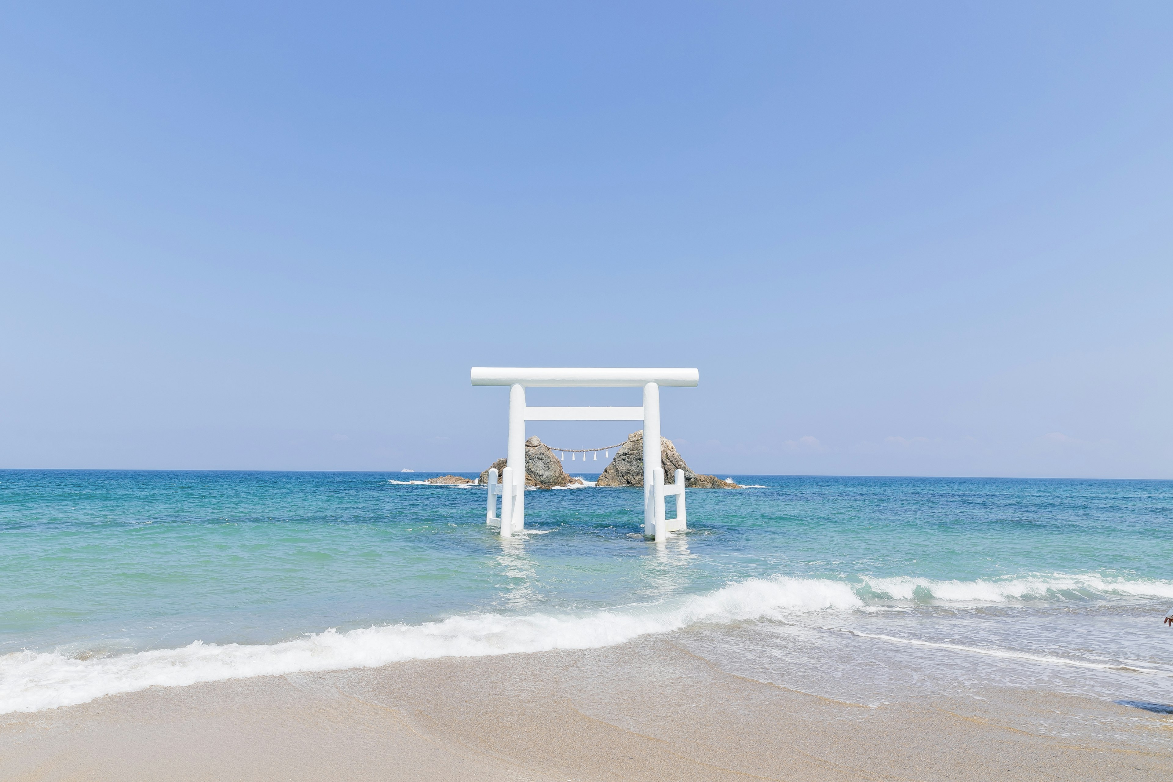 Escena de playa con un océano azul y una puerta torii blanca