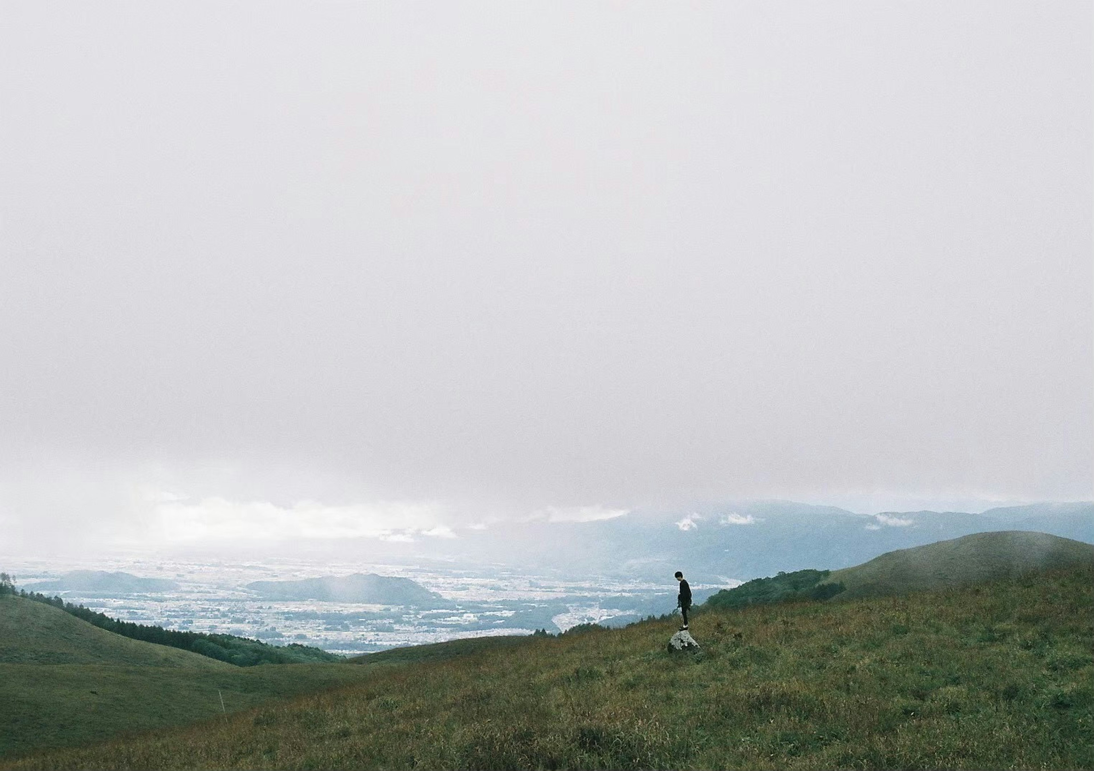 Person steht in einer weiten grasbewachsenen Landschaft mit nebligen Bergen