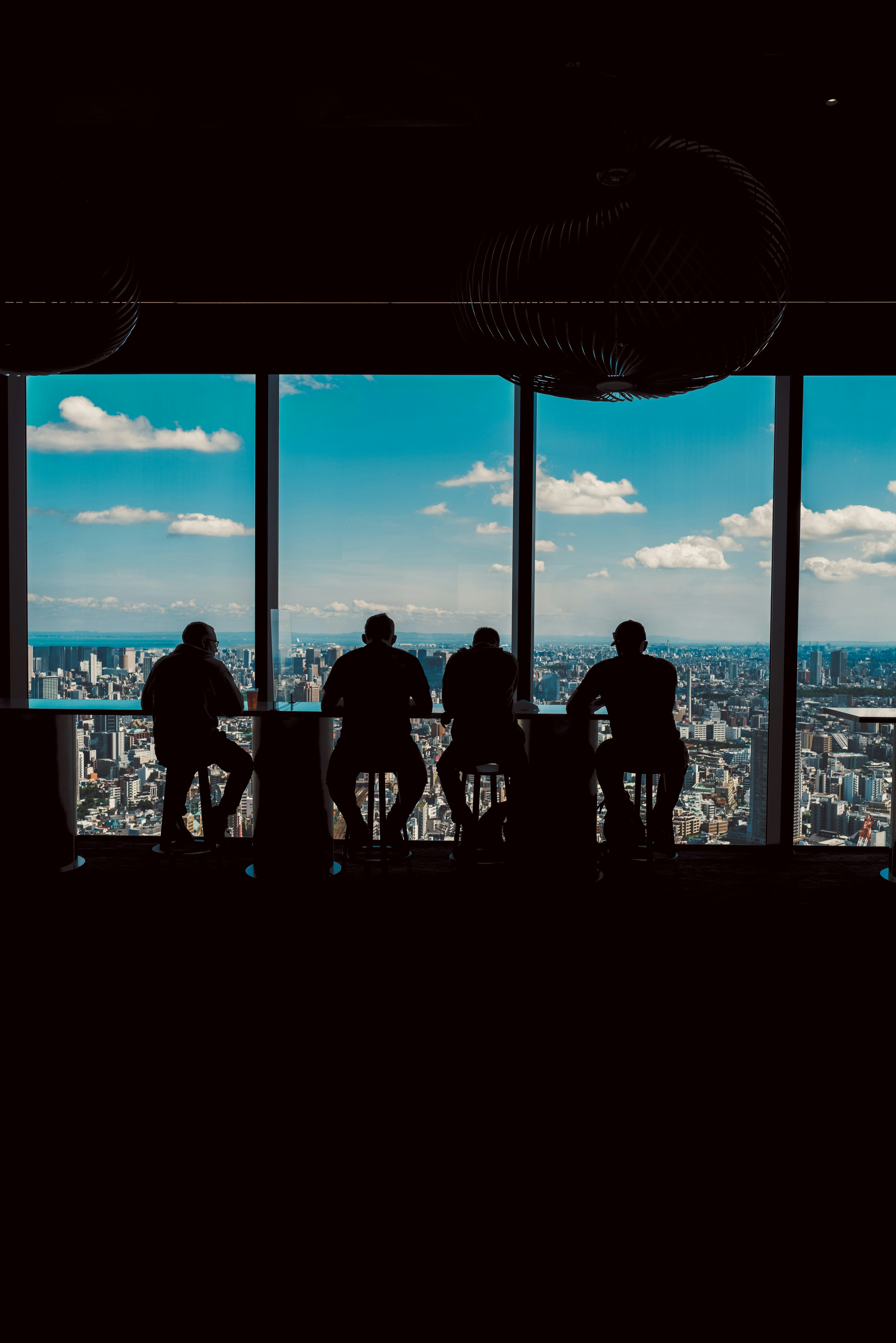 Four silhouettes of people sitting by a window overlooking a cityscape