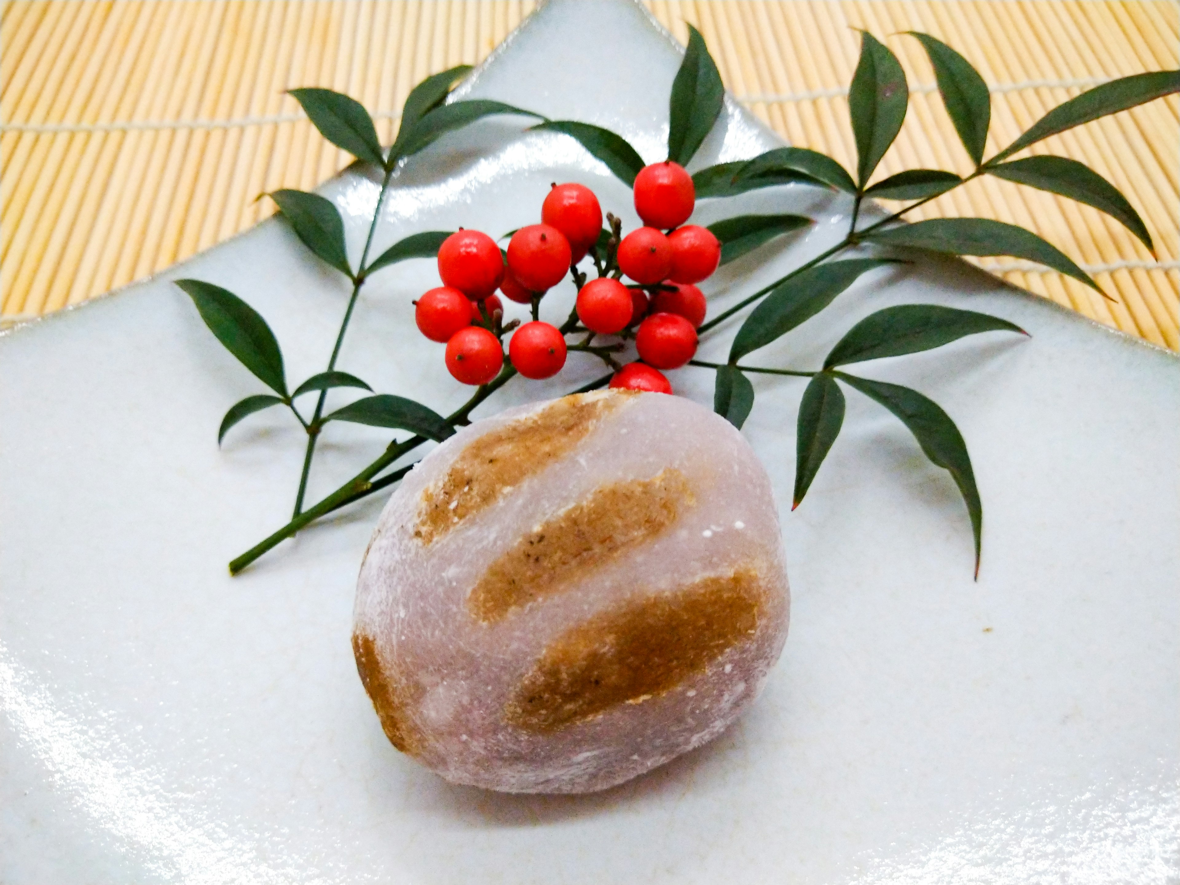 A traditional Japanese sweet on a white plate decorated with red berries and green leaves