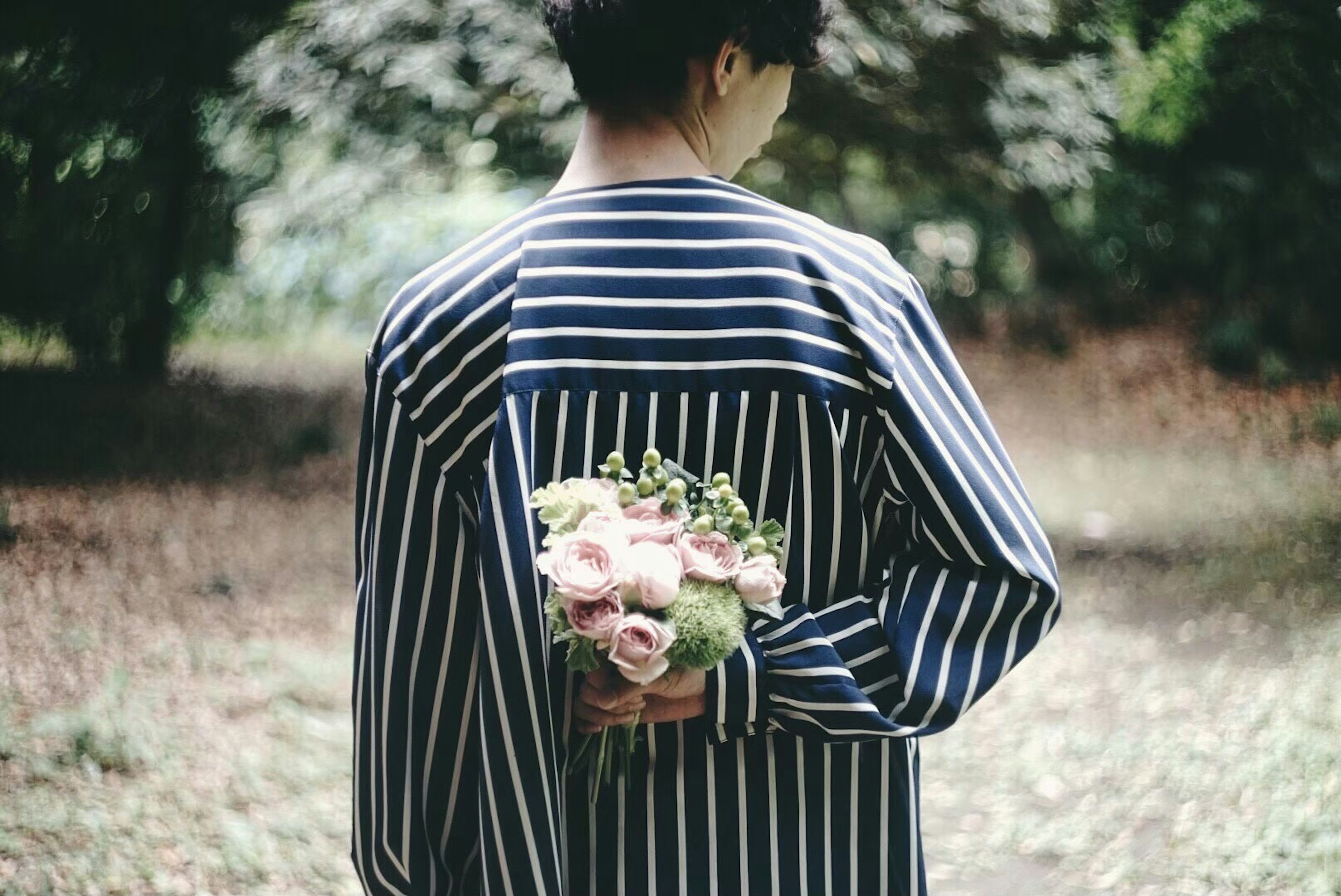 Persona con camisa de rayas sosteniendo un ramo de flores detrás de la espalda