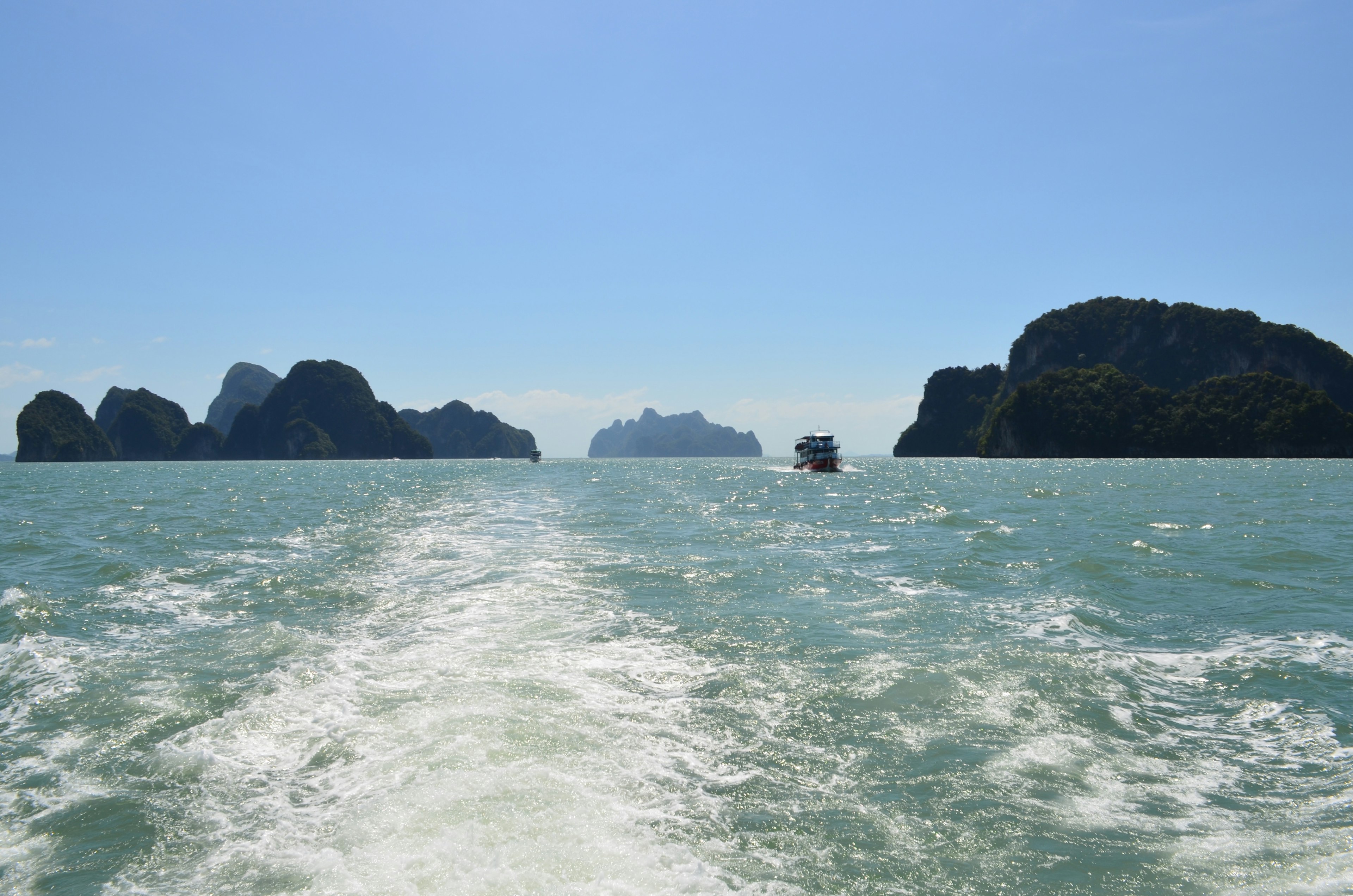 Pemandangan laut biru dengan pulau berbatu jejak kapal terlihat di air