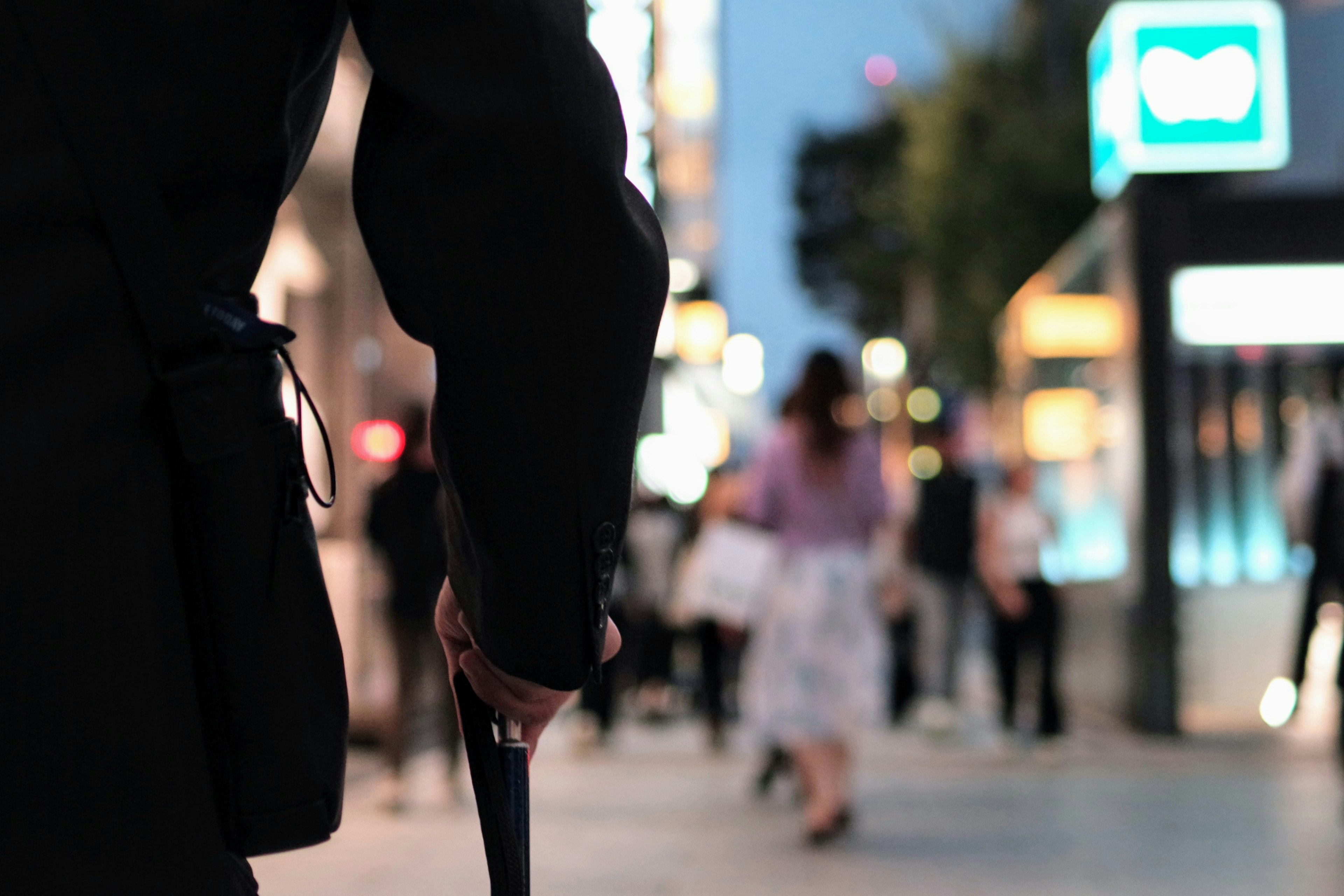 夜の都市の通りを歩く人々を背景にした黒いコートを着た人物の後ろ姿