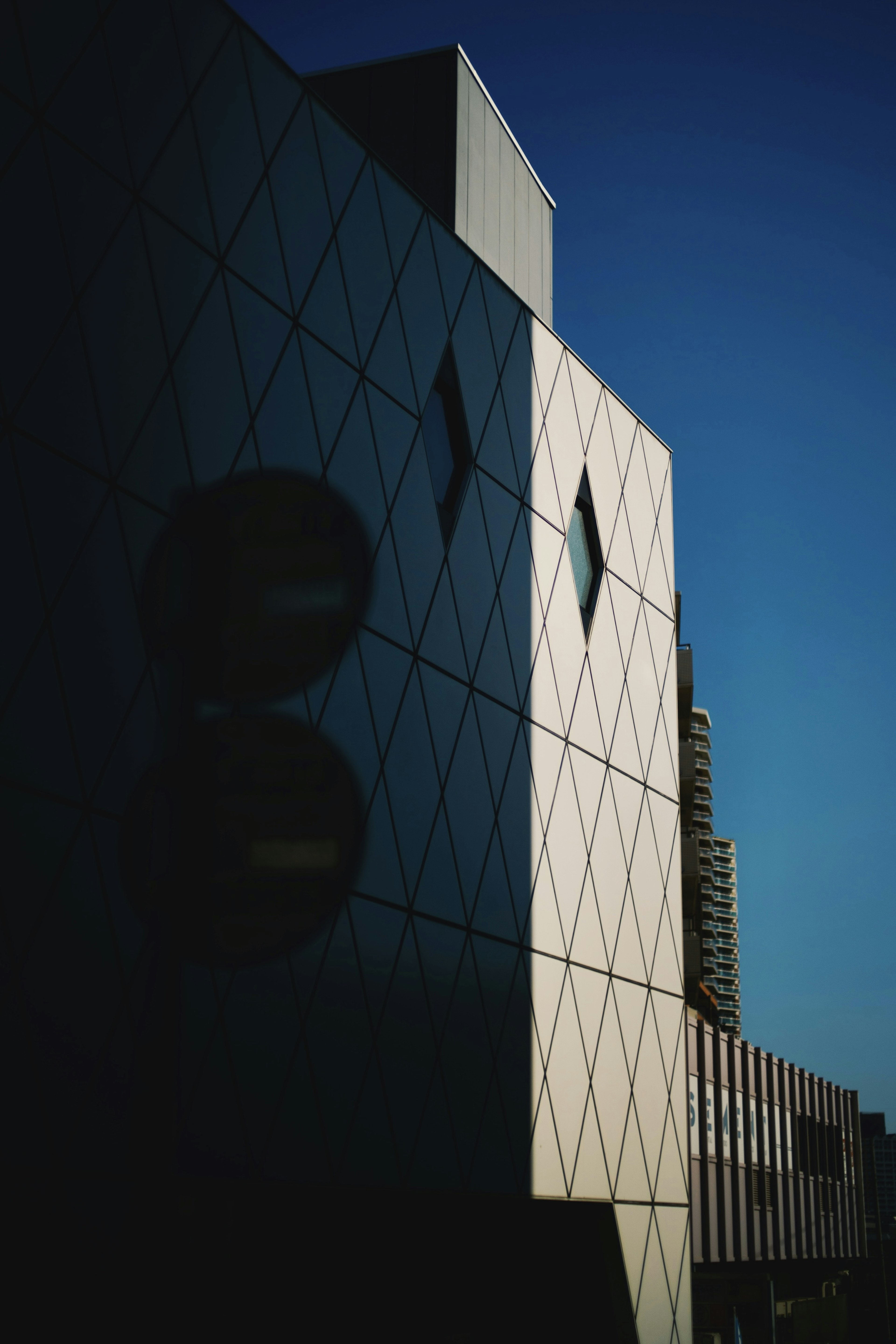 Façade d'un bâtiment moderne se reflétant sous un ciel bleu avec un design angulaire et des reflets distinctifs