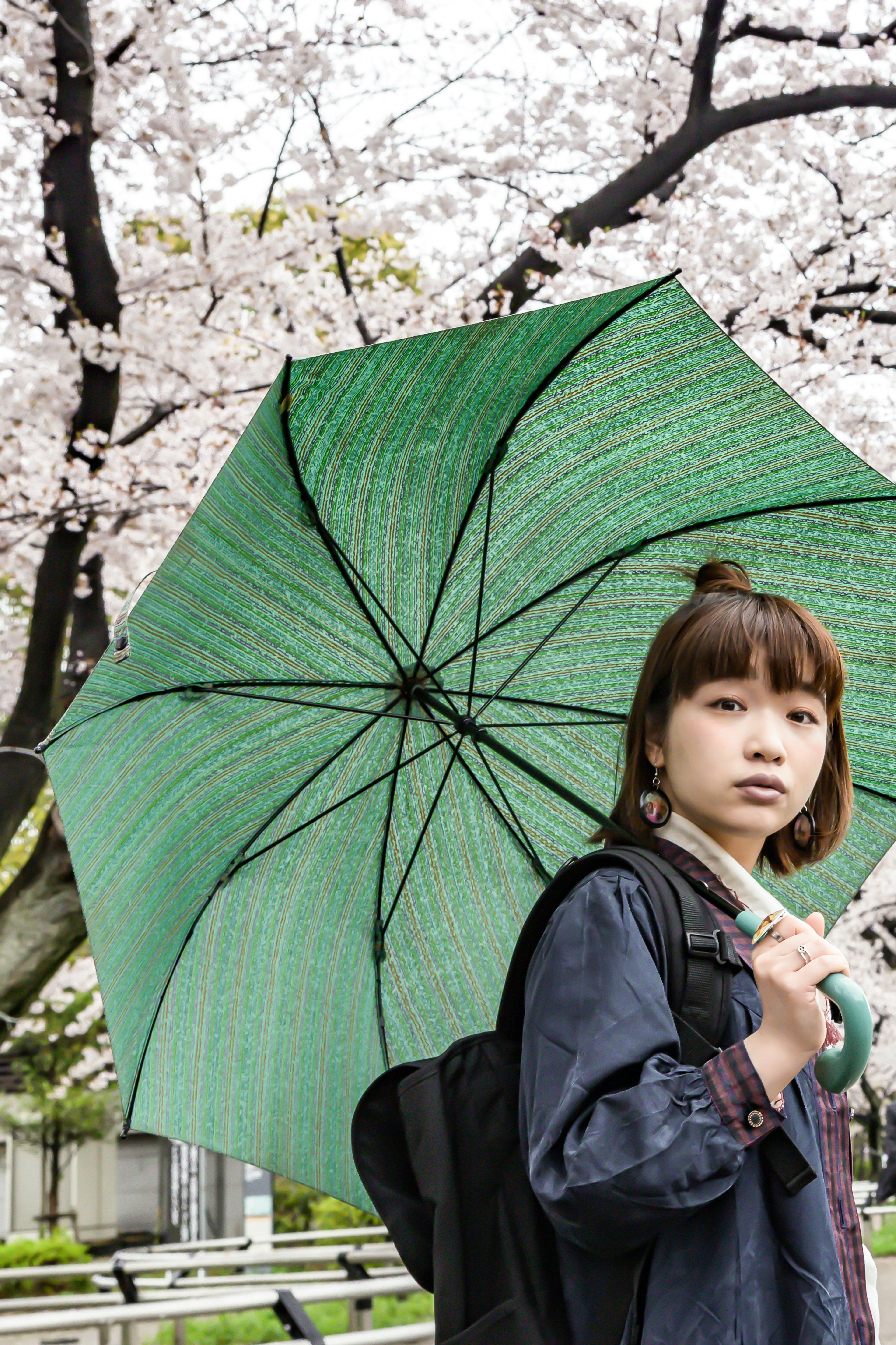 Femme tenant un parapluie vert sous des cerisiers en fleurs