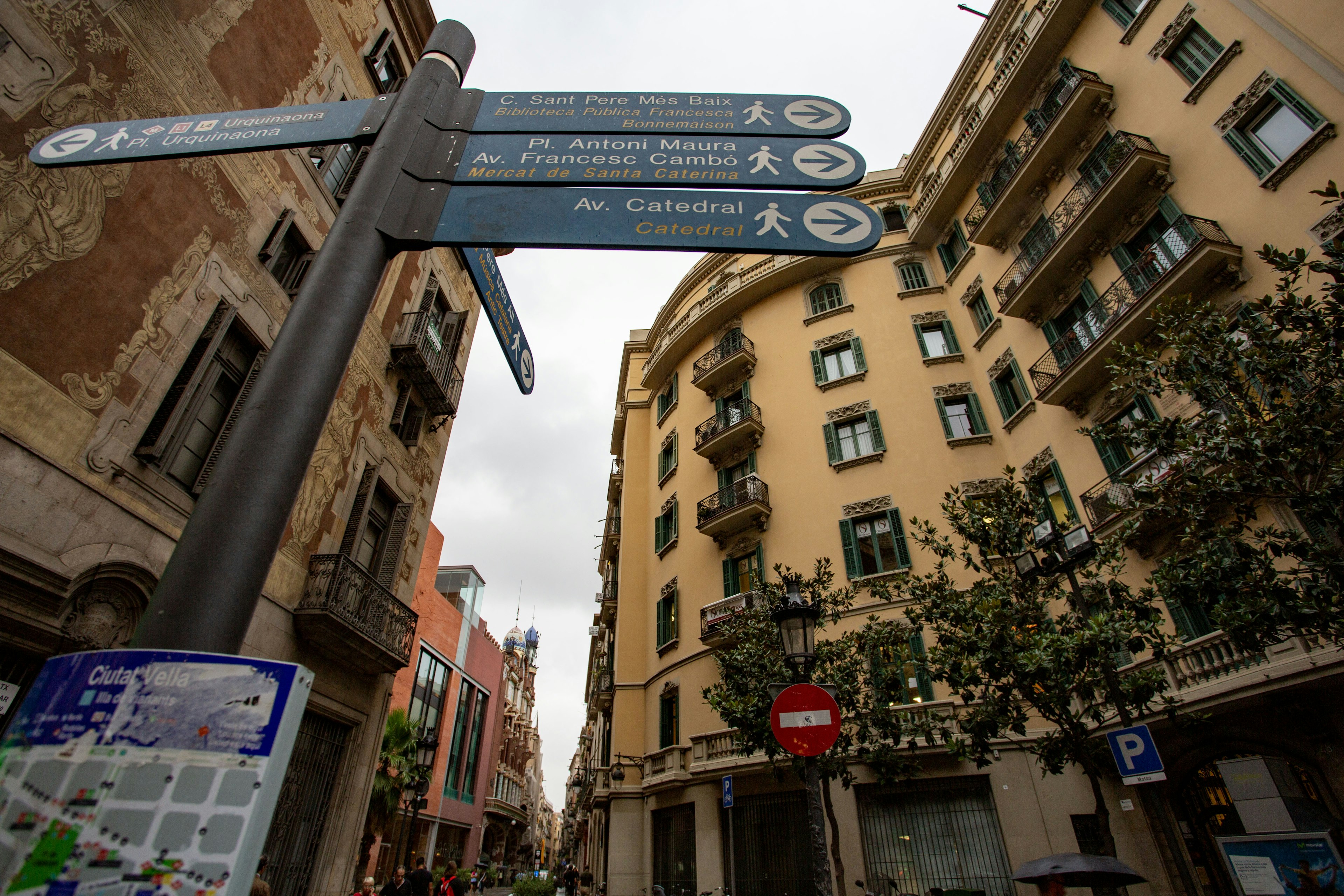 Papan jalan di Barcelona dengan panah arah dan bangunan bersejarah