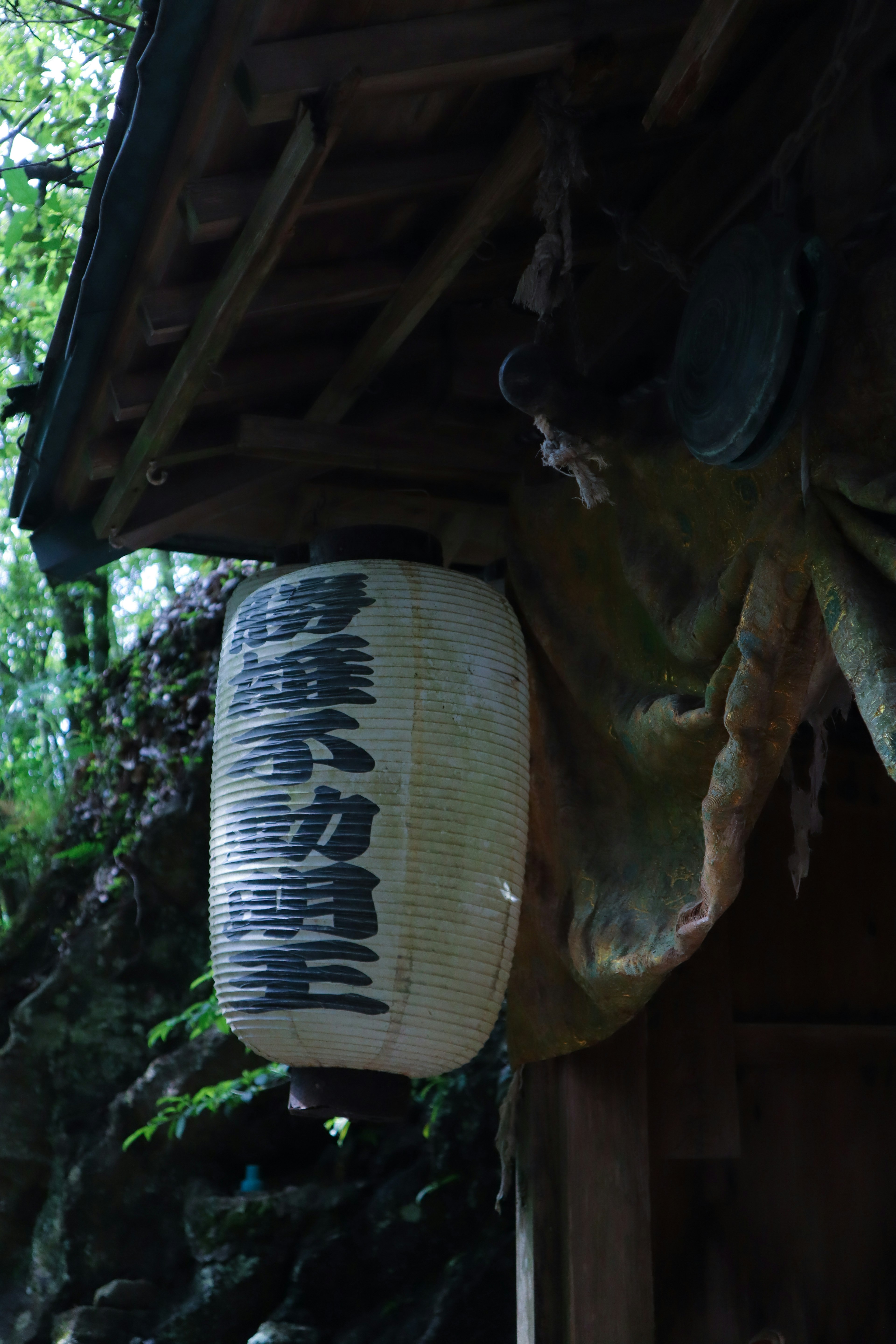 Japanese lantern hanging under a wooden roof featuring kanji characters