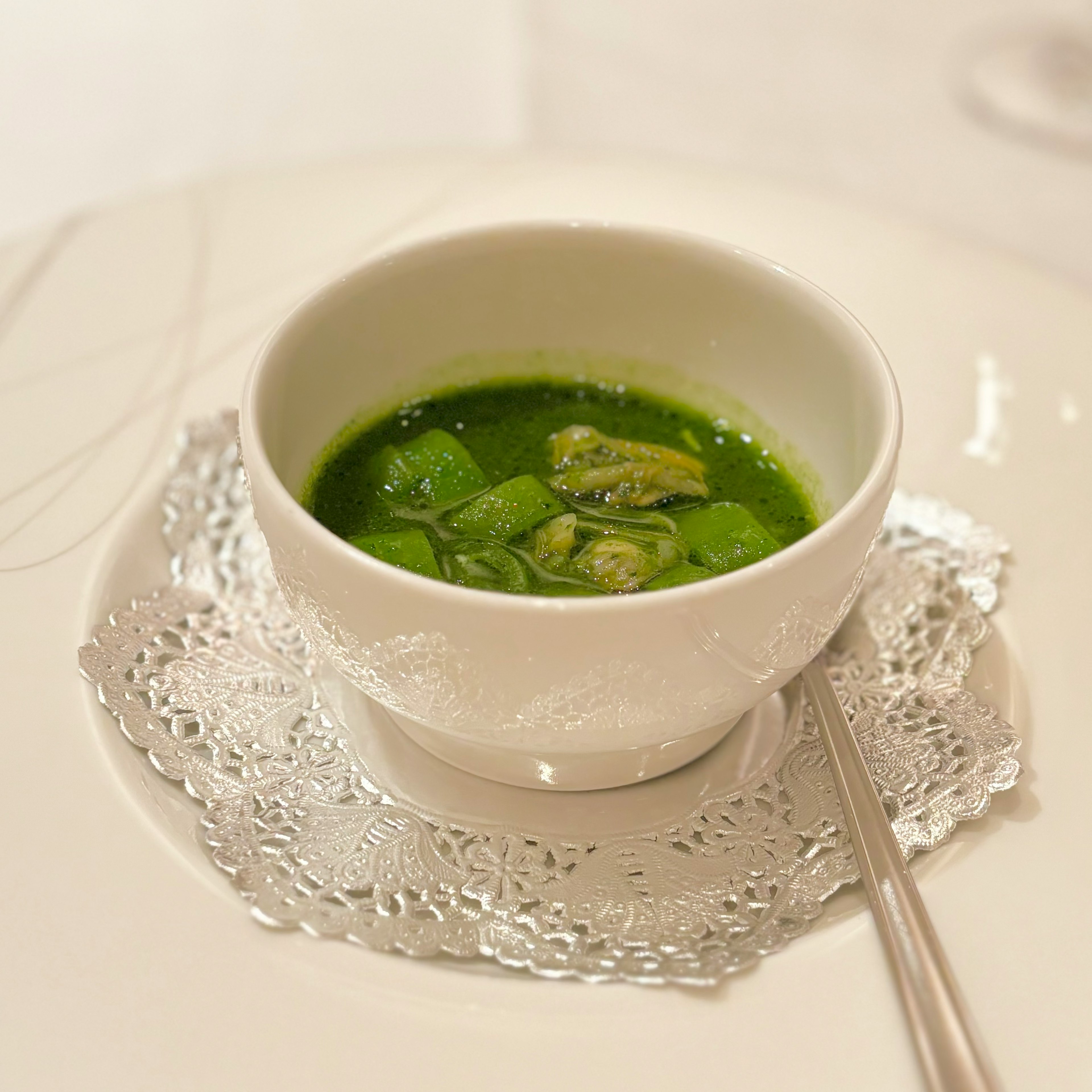 Green soup in a white bowl placed on a delicate lace plate