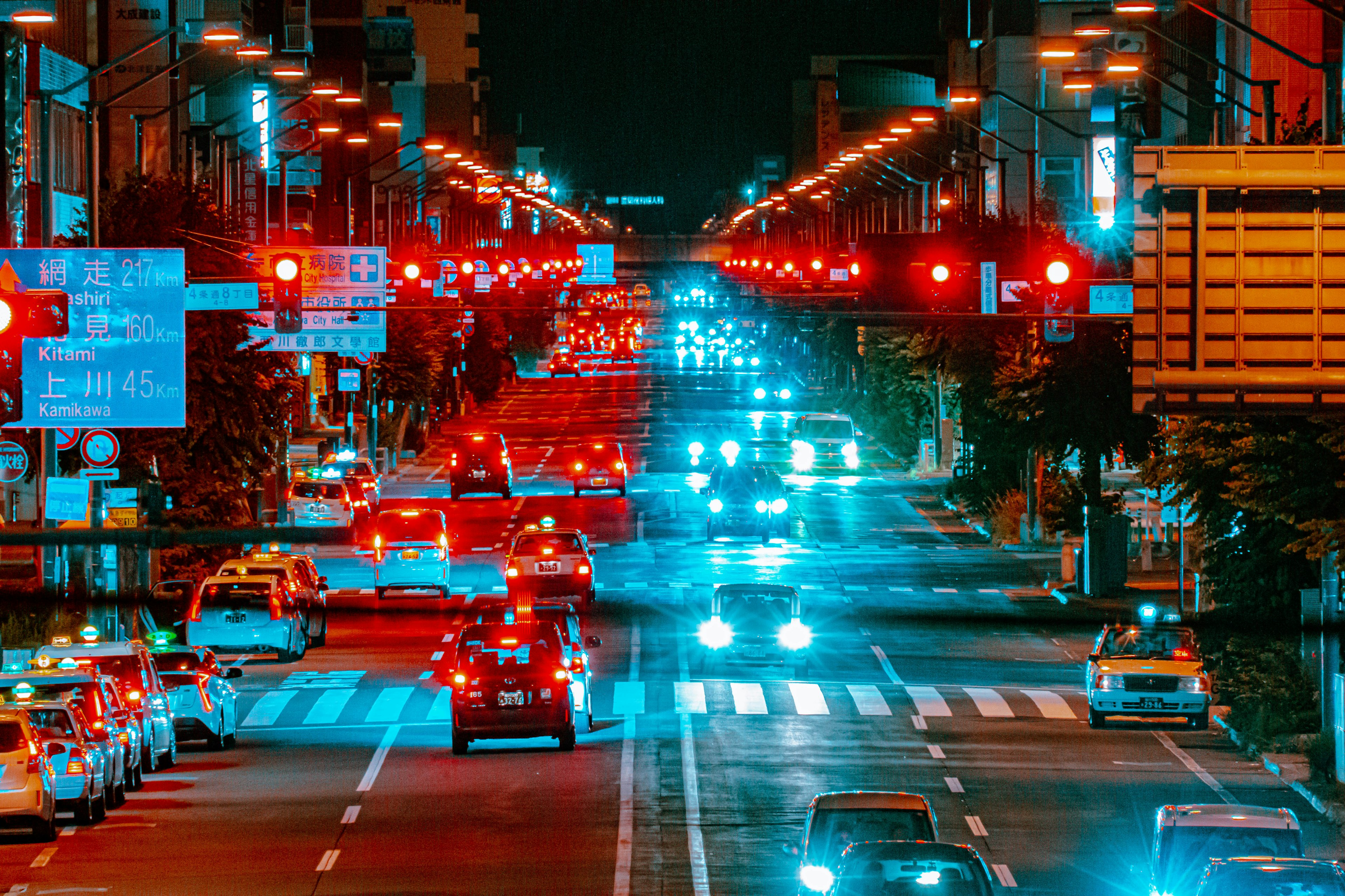 Night city intersection with glowing car headlights and taillights prominent red traffic lights