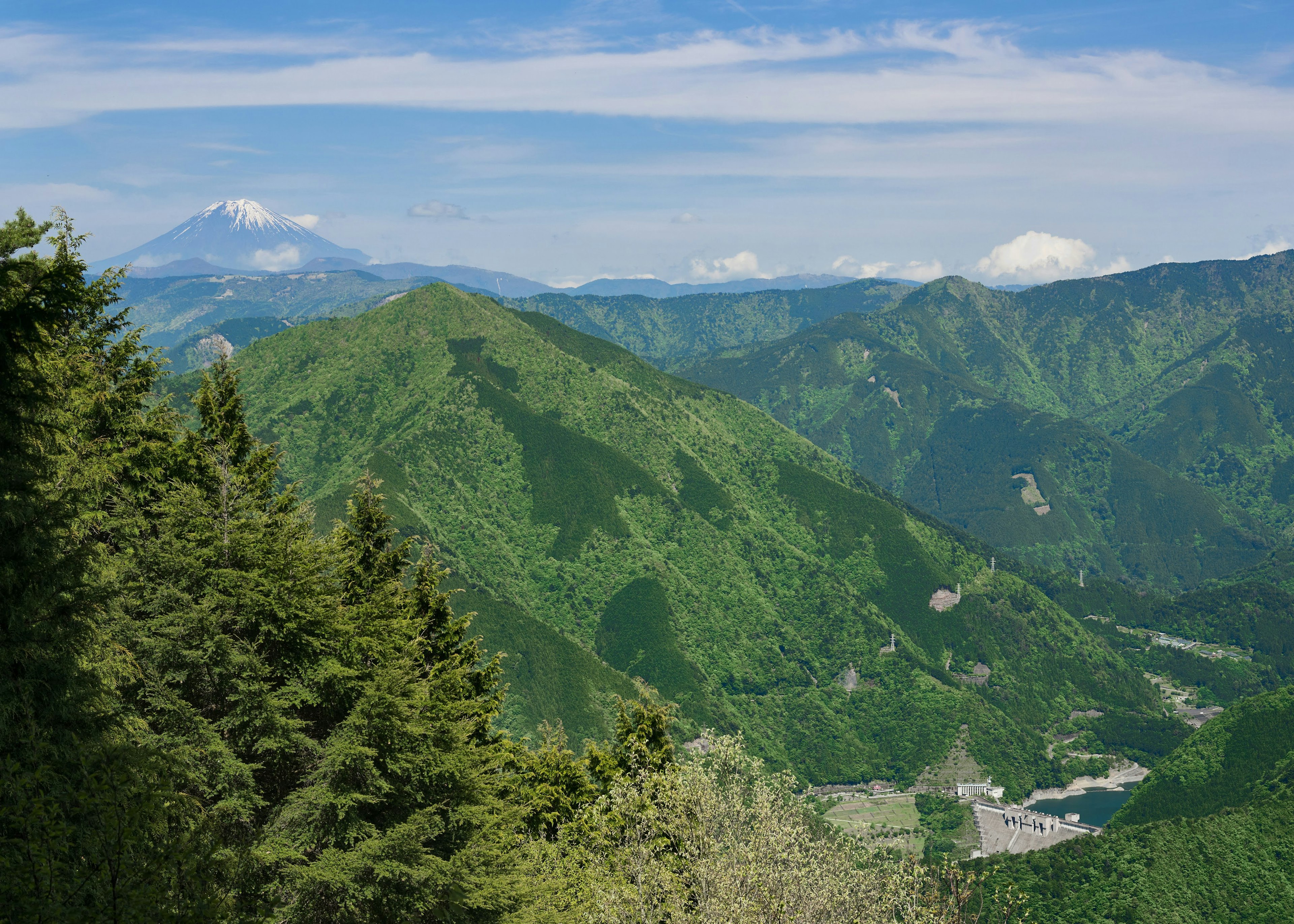 郁郁葱葱的绿色山脉和晴朗的蓝天，远处可见富士山