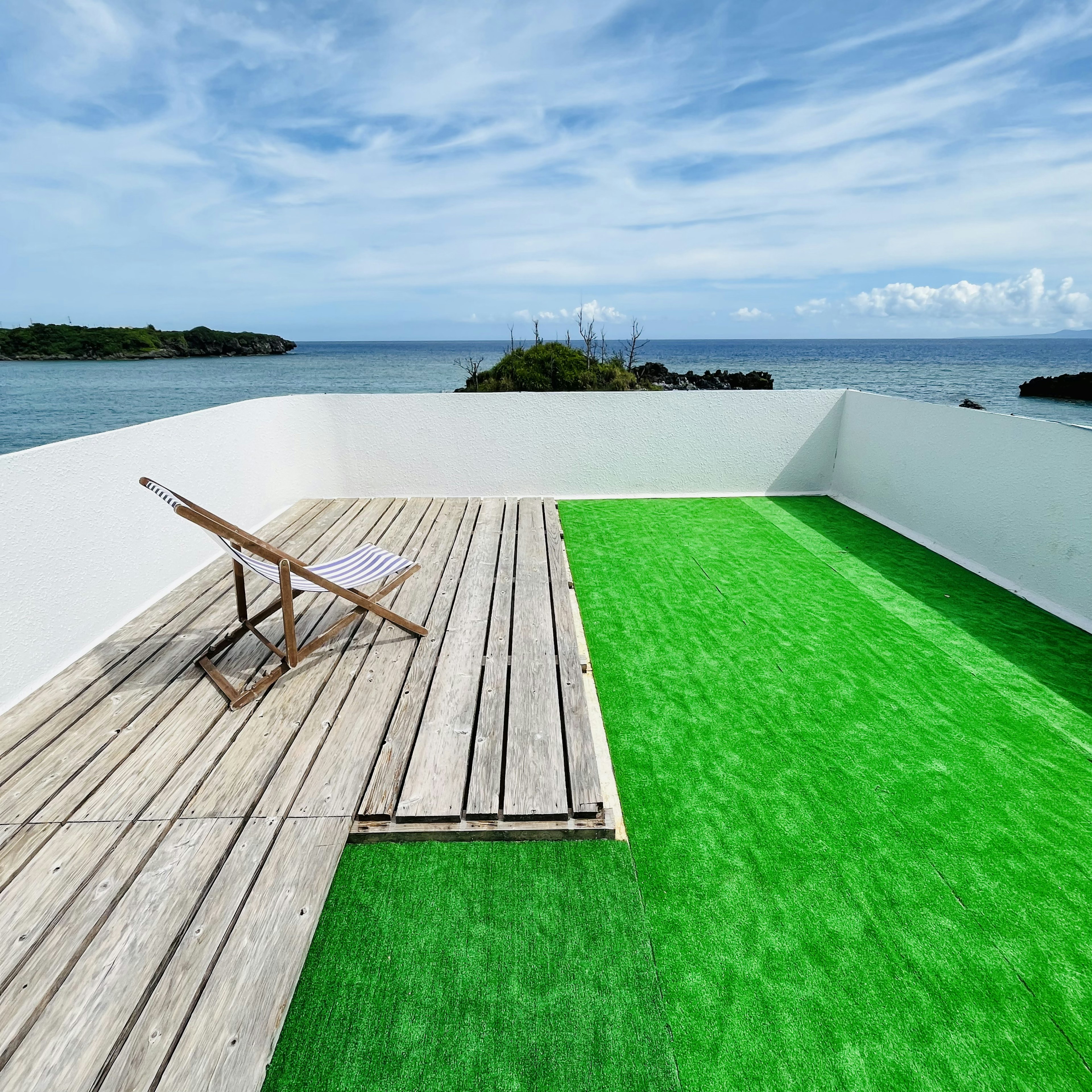 Toit-terrasse avec gazon vert et terrasse en bois surplombant la mer bleue et le ciel