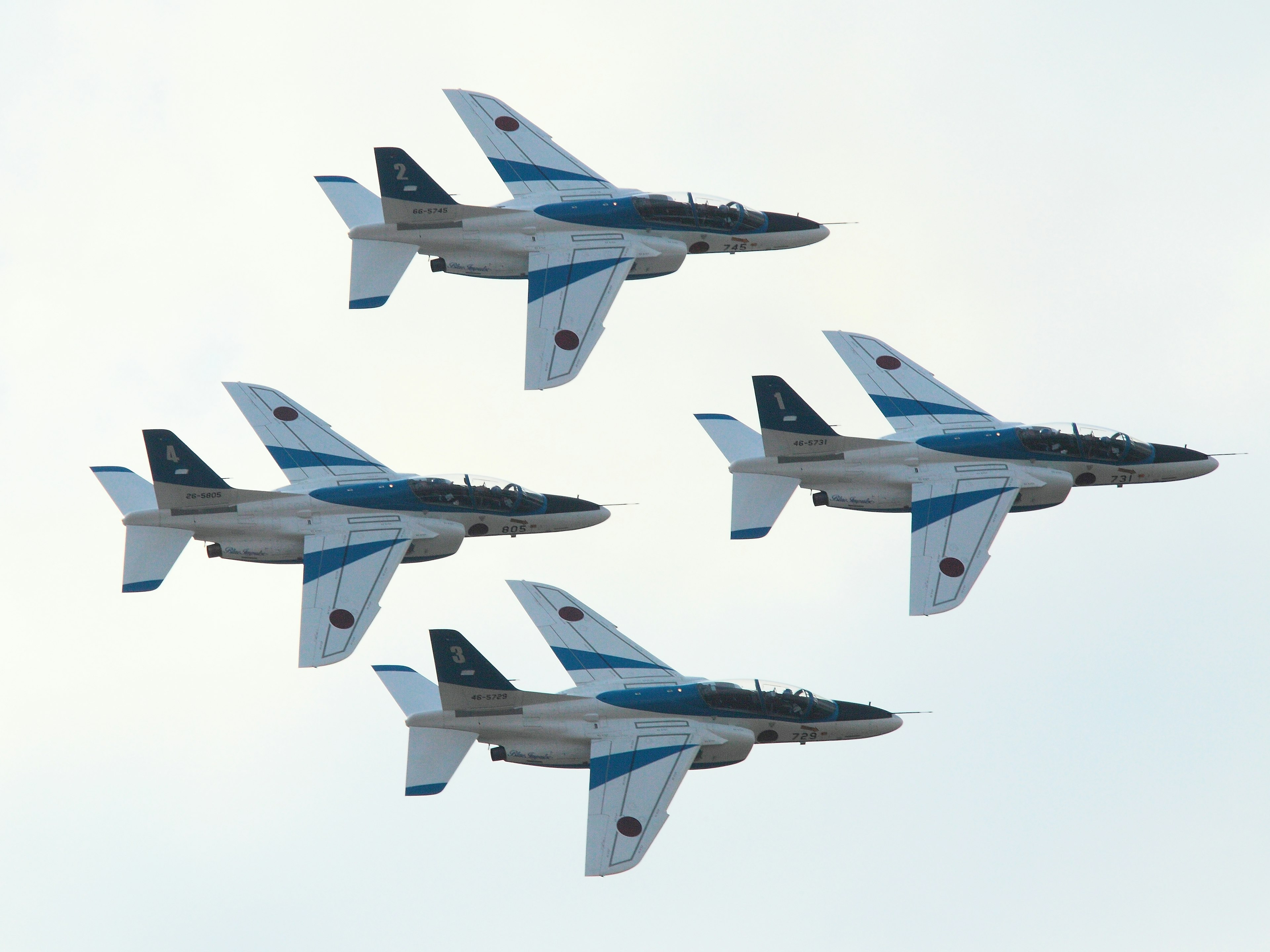 Four military jets in blue and white flying in formation against a cloudy sky