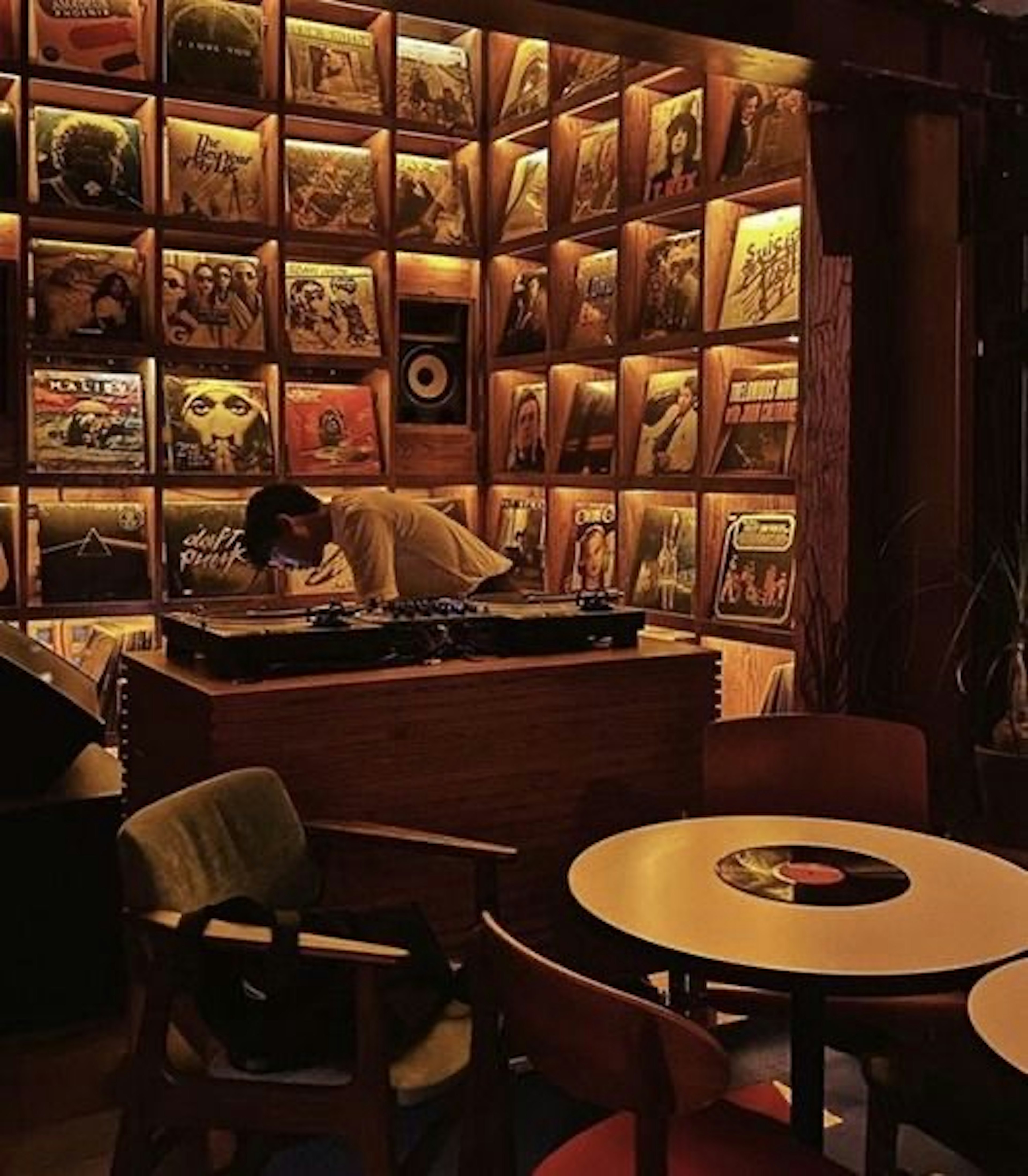 Un DJ trabajando en un café con una pared de discos de vinilo