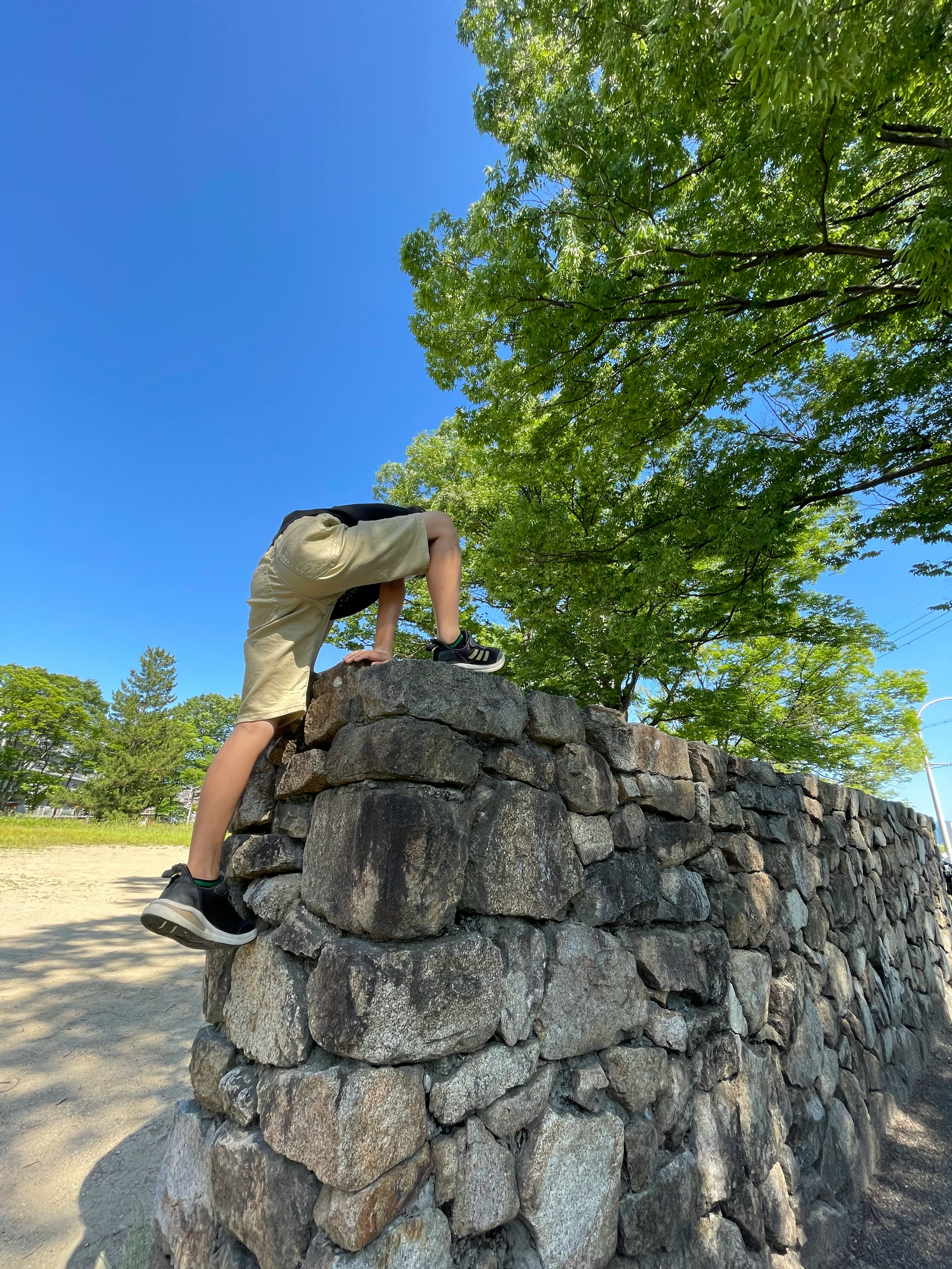 青空の下で石の壁に登っている少年