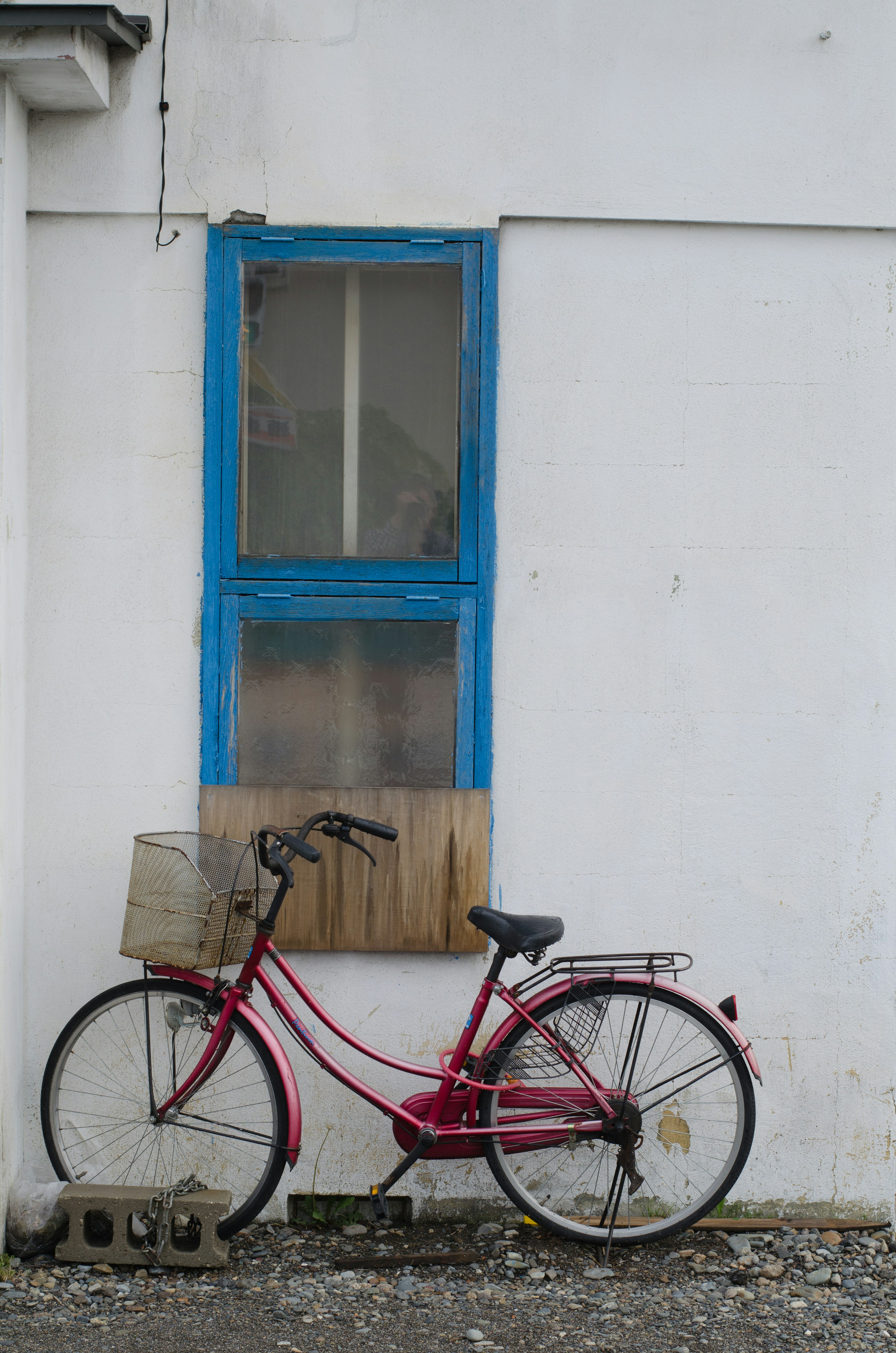 A red bicycle stands in front of a white wall with a blue window