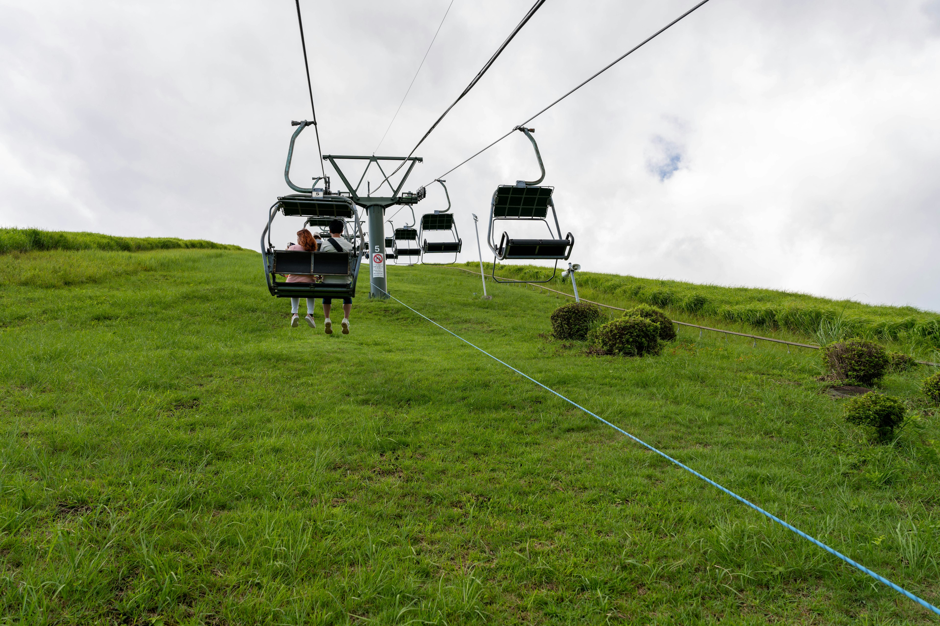 Ski lift on a green hill with cloudy sky