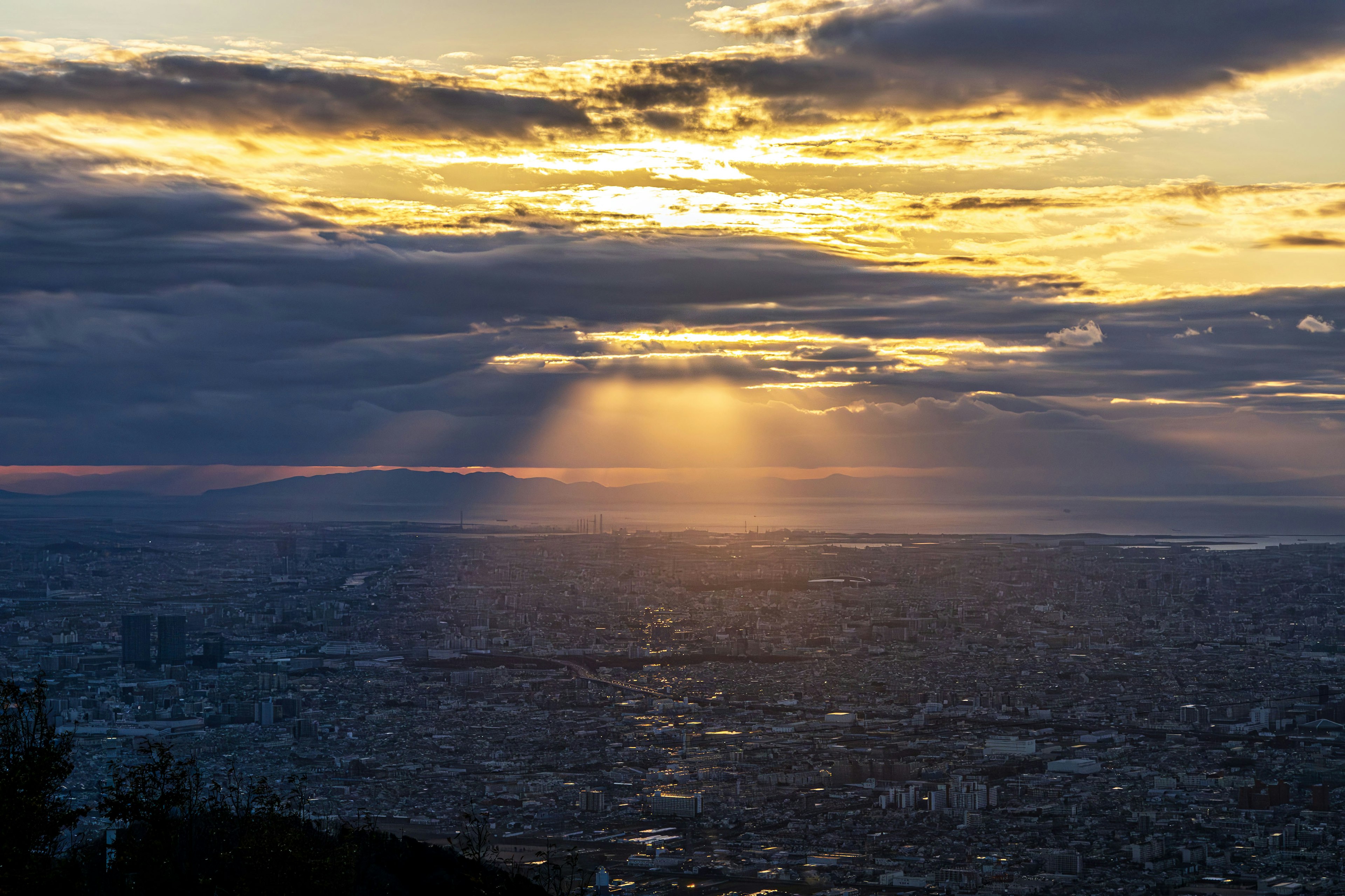 Vista panoramica di una città al tramonto con raggi di luce che filtrano tra le nuvole